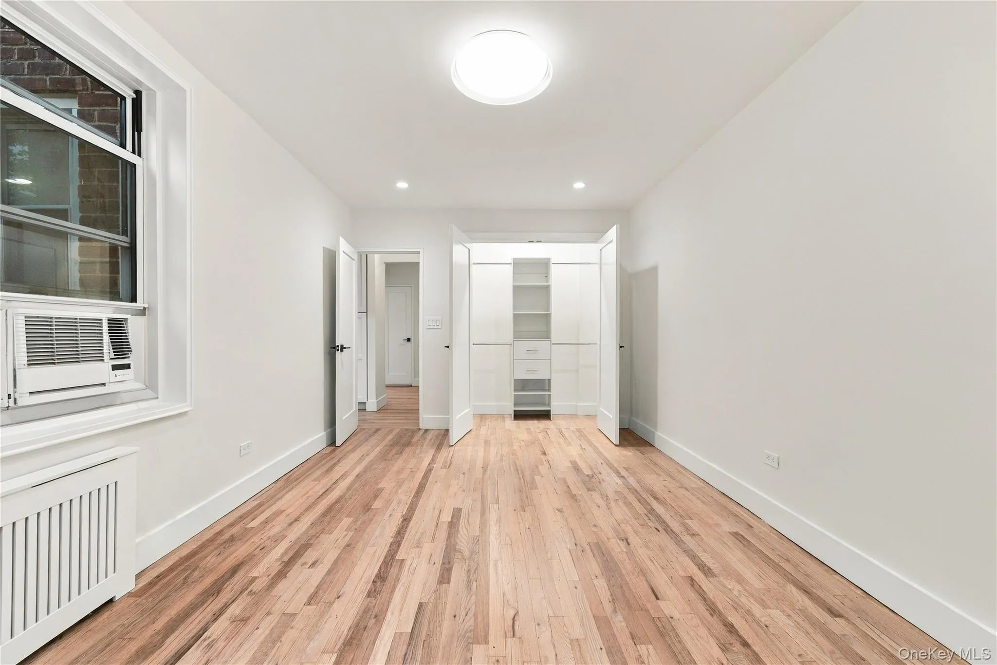 Room featuring wood-finish flooring, recessed lighting, and built-in white cabinetry with integrated shelving and drawers Room featuring wood-finish flooring, recessed lighting, and built-in white cabinetry with integrated shelving and drawers