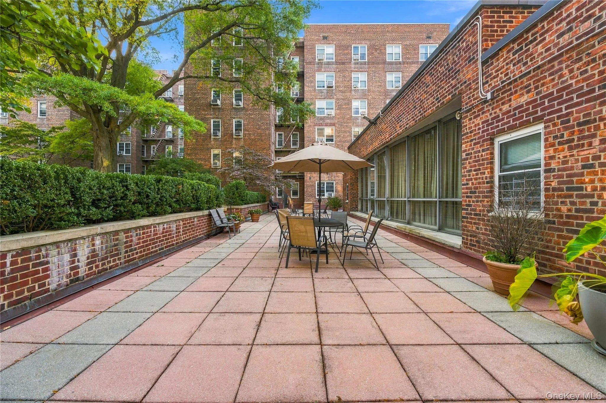 Spacious exterior terrace featuring red brick masonry walls, paved tile flooring, and perimeter hedge landscaping Spacious exterior terrace featuring red brick masonry walls, paved tile flooring, and perimeter hedge landscaping