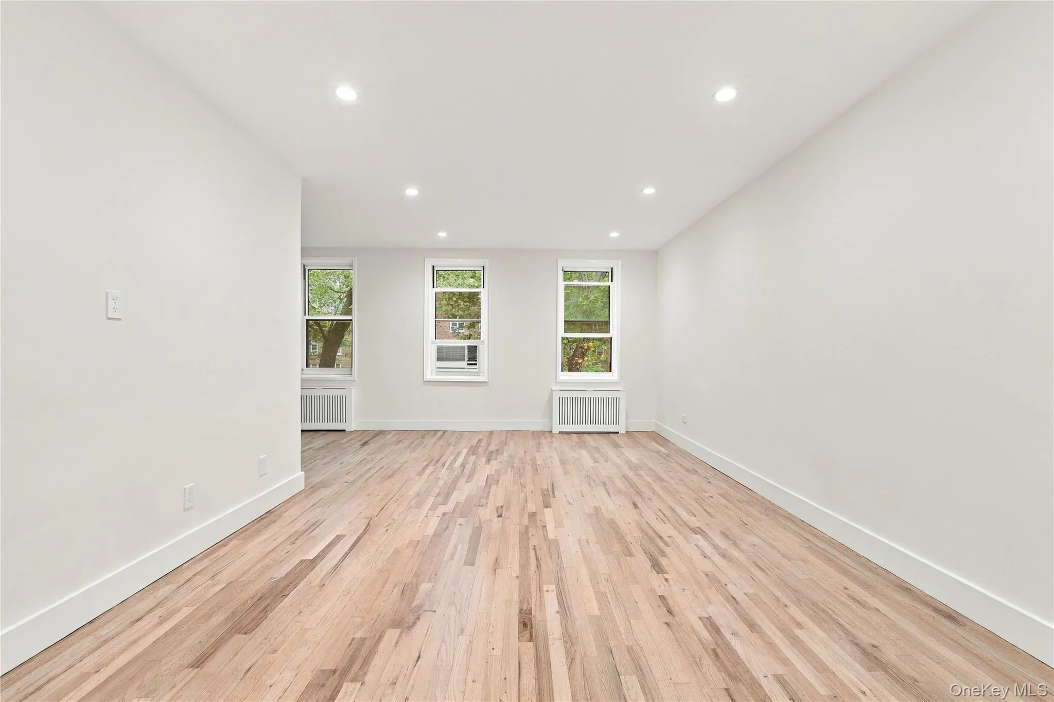 Interior space featuring wood-finish flooring, neutral white walls, recessed ceiling lighting, and triple window configuration Interior space featuring wood-finish flooring, neutral white walls, recessed ceiling lighting, and triple window configuration