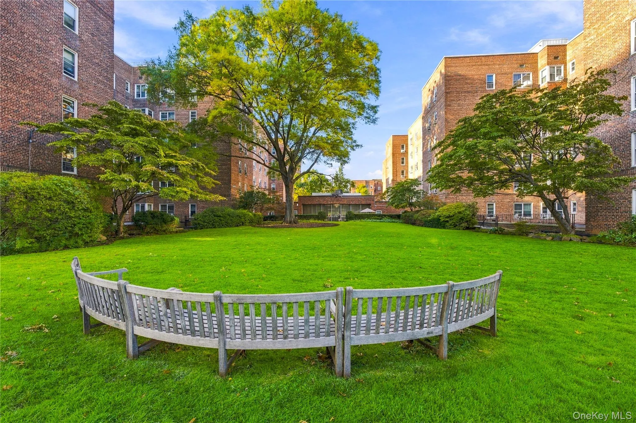 Landscaped courtyard featuring mature trees, peripheral brick facades, and a curved wooden bench Landscaped courtyard featuring mature trees, peripheral brick facades, and a curved wooden bench