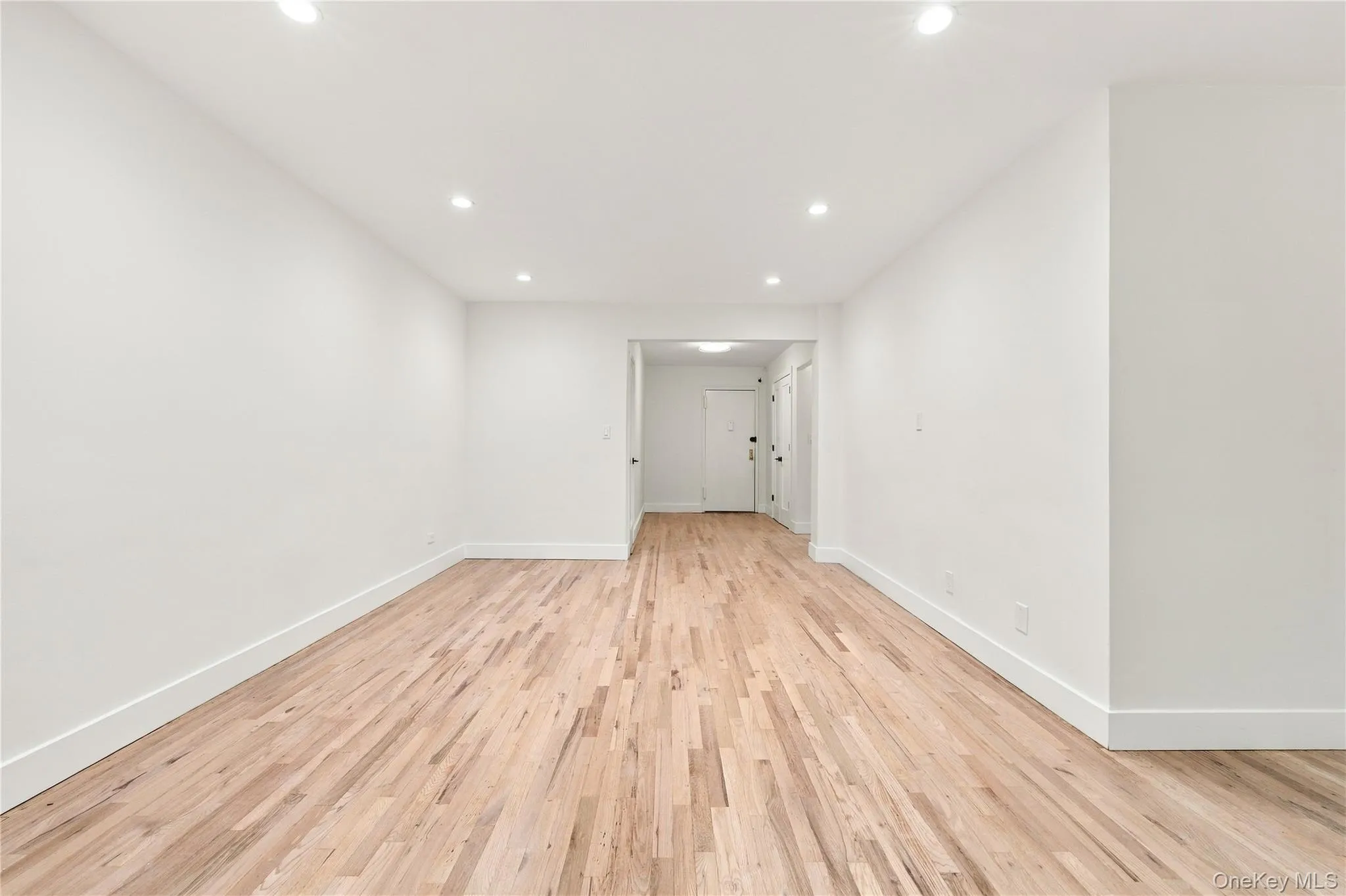 Interior space featuring wood-finish flooring, white walls, and recessed ceiling lighting Interior space featuring wood-finish flooring, white walls, and recessed ceiling lighting