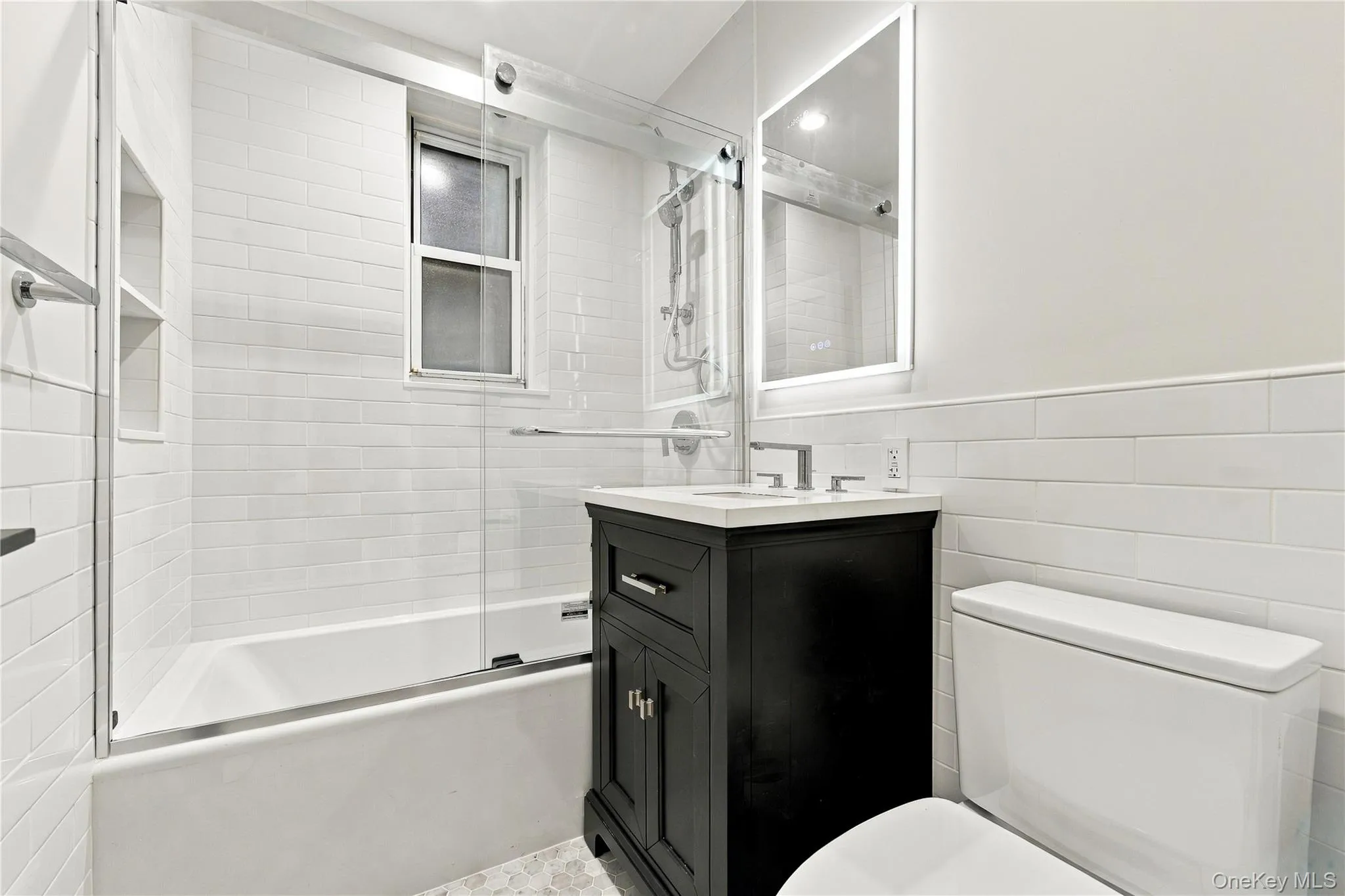Bathroom featuring a dark wood vanity with a stone countertop, a glass-enclosed tub with subway tile surround, an integrated wall niche, and an illuminated mirror Bathroom featuring a dark wood vanity with a stone countertop, a glass-enclosed tub with subway tile surround, an integrated wall niche, and an illuminated mirror