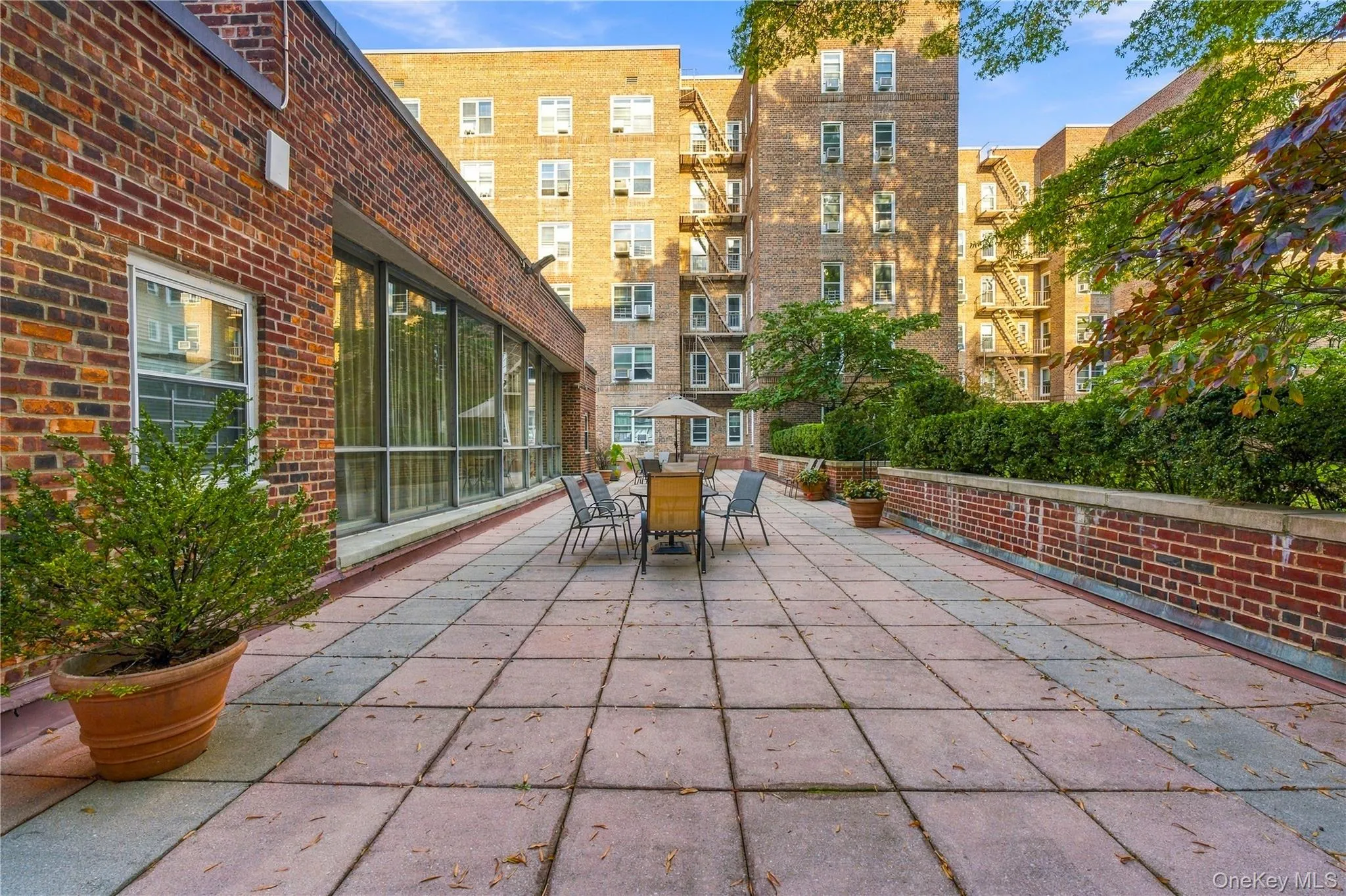 Expansive brick-paved patio featuring a surrounding masonry wall, large floor-to-ceiling windows, and mature perimeter landscaping Expansive brick-paved patio featuring a surrounding masonry wall, large floor-to-ceiling windows, and mature perimeter landscaping