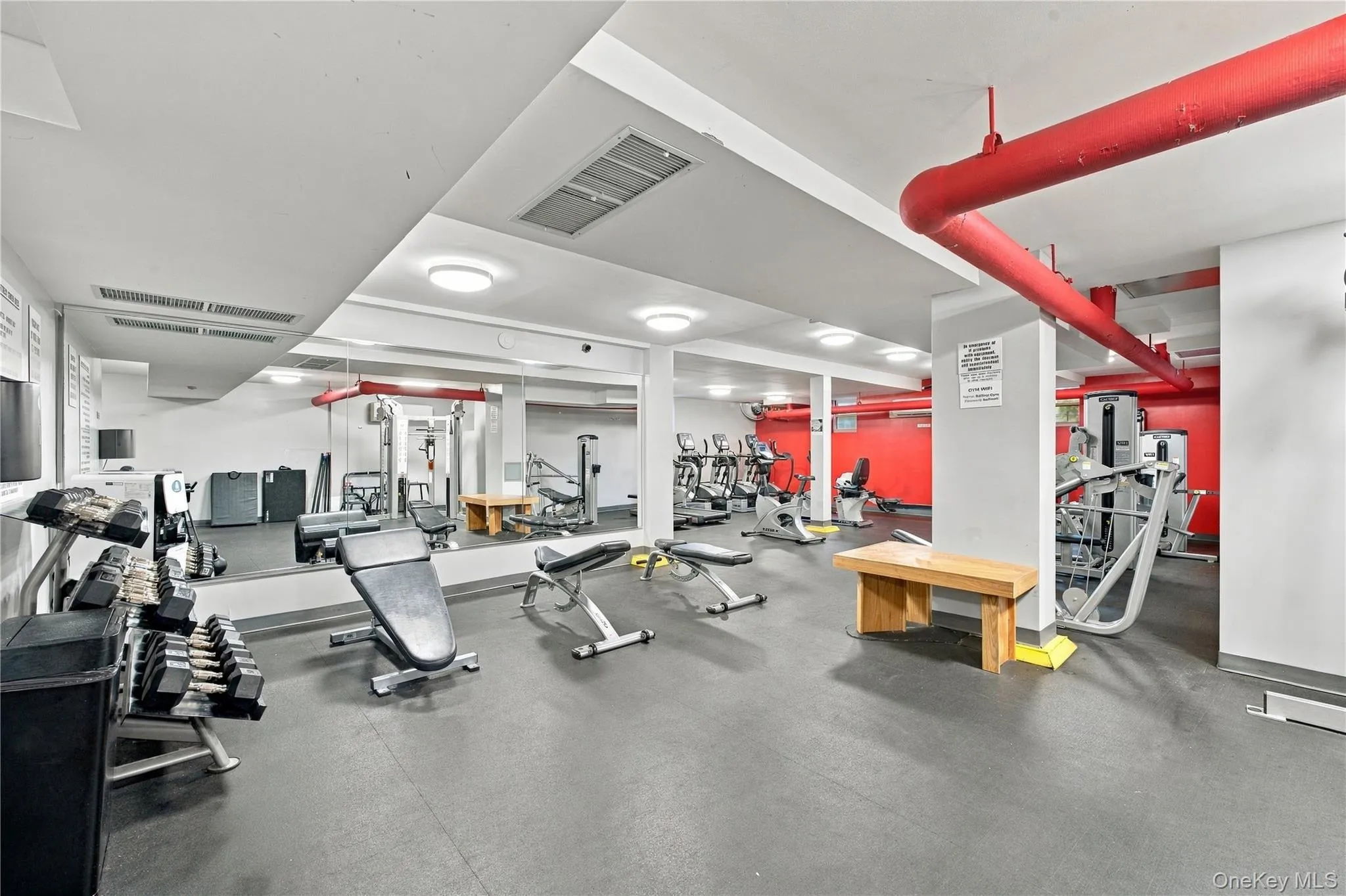 Fitness center featuring rubberized flooring, expansive wall-to-wall mirrors, recessed lighting, and exposed overhead piping Fitness center featuring rubberized flooring, expansive wall-to-wall mirrors, recessed lighting, and exposed overhead piping