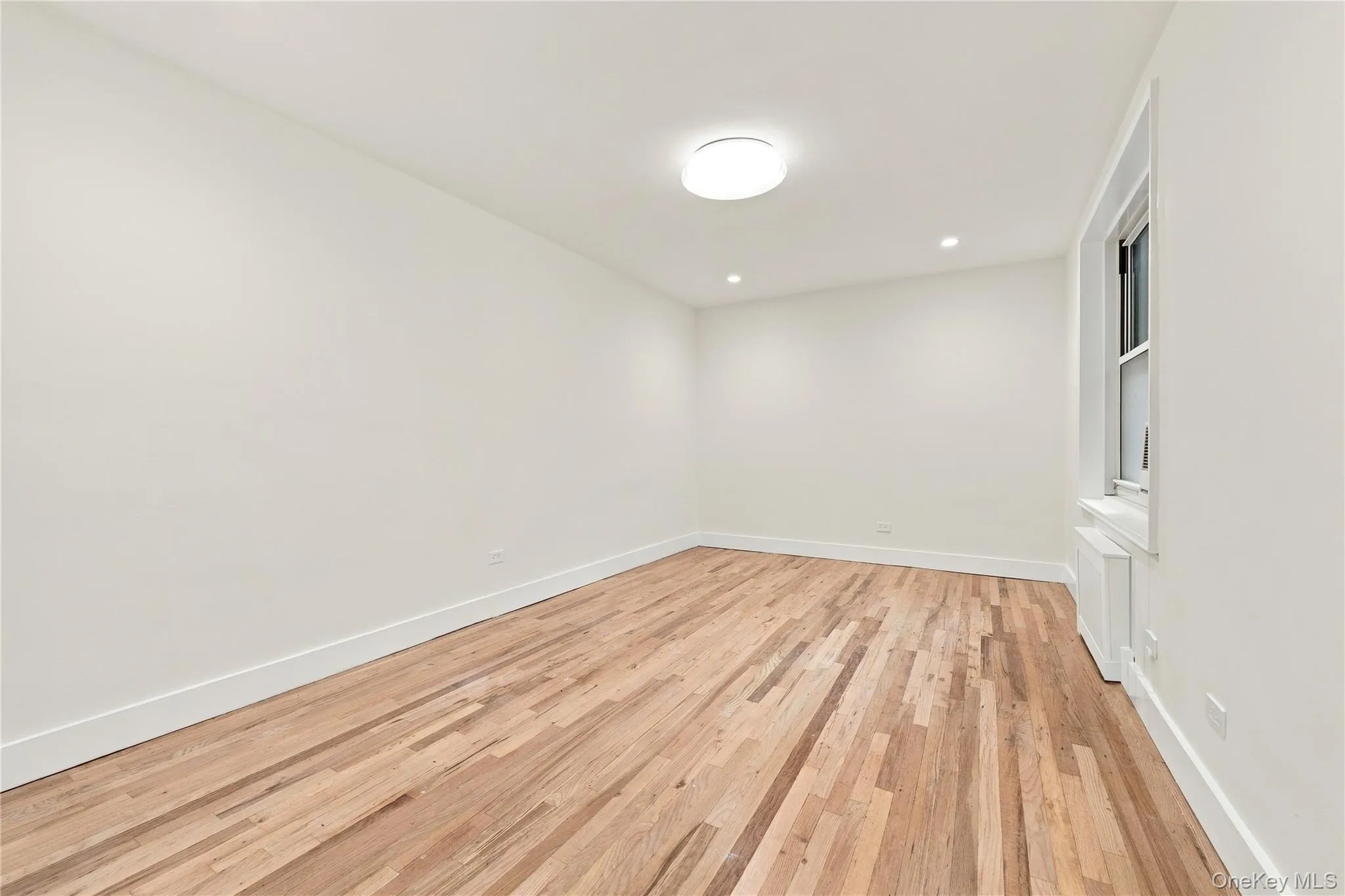 Interior space featuring wood-finish flooring, white walls, flush-mount overhead lighting, recessed lighting, and a window with a white frame Interior space featuring wood-finish flooring, white walls, flush-mount overhead lighting, recessed lighting, and a window with a white frame