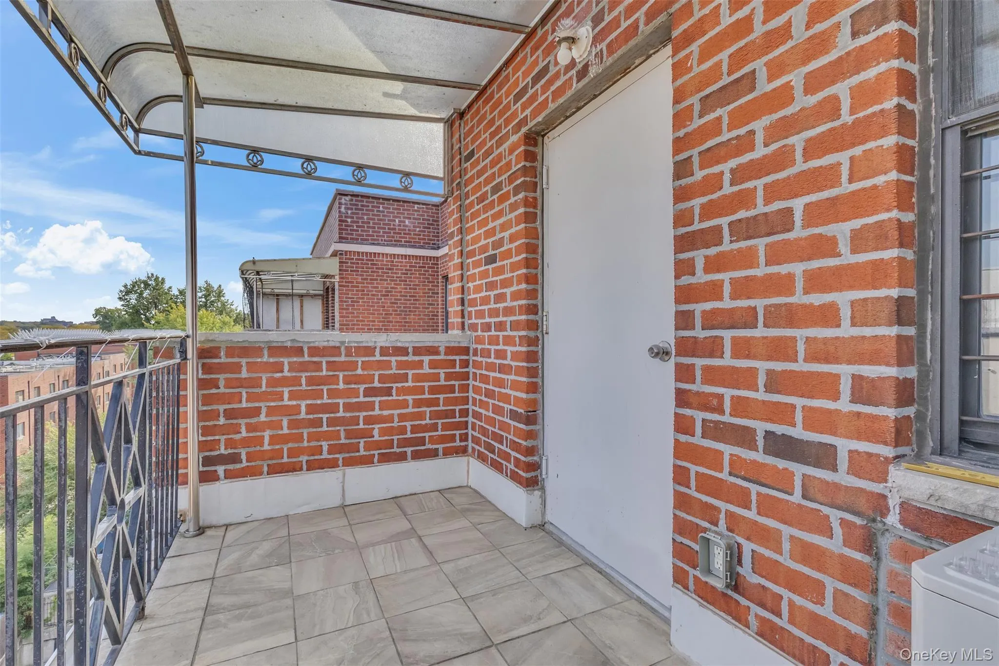 Balcony featuring red brick exterior walls, stone-finish tile flooring, metal railing, and a fixed overhead awning Balcony featuring red brick exterior walls, stone-finish tile flooring, metal railing, and a fixed overhead awning