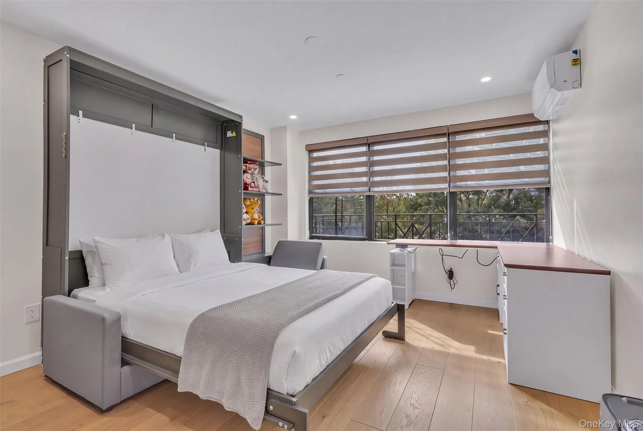 Built-in dark-toned cabinetry with integrated shelving, wood-finish flooring, recessed lighting, and wall-mounted climate control unit Built-in dark-toned cabinetry with integrated shelving, wood-finish flooring, recessed lighting, and wall-mounted climate control unit
