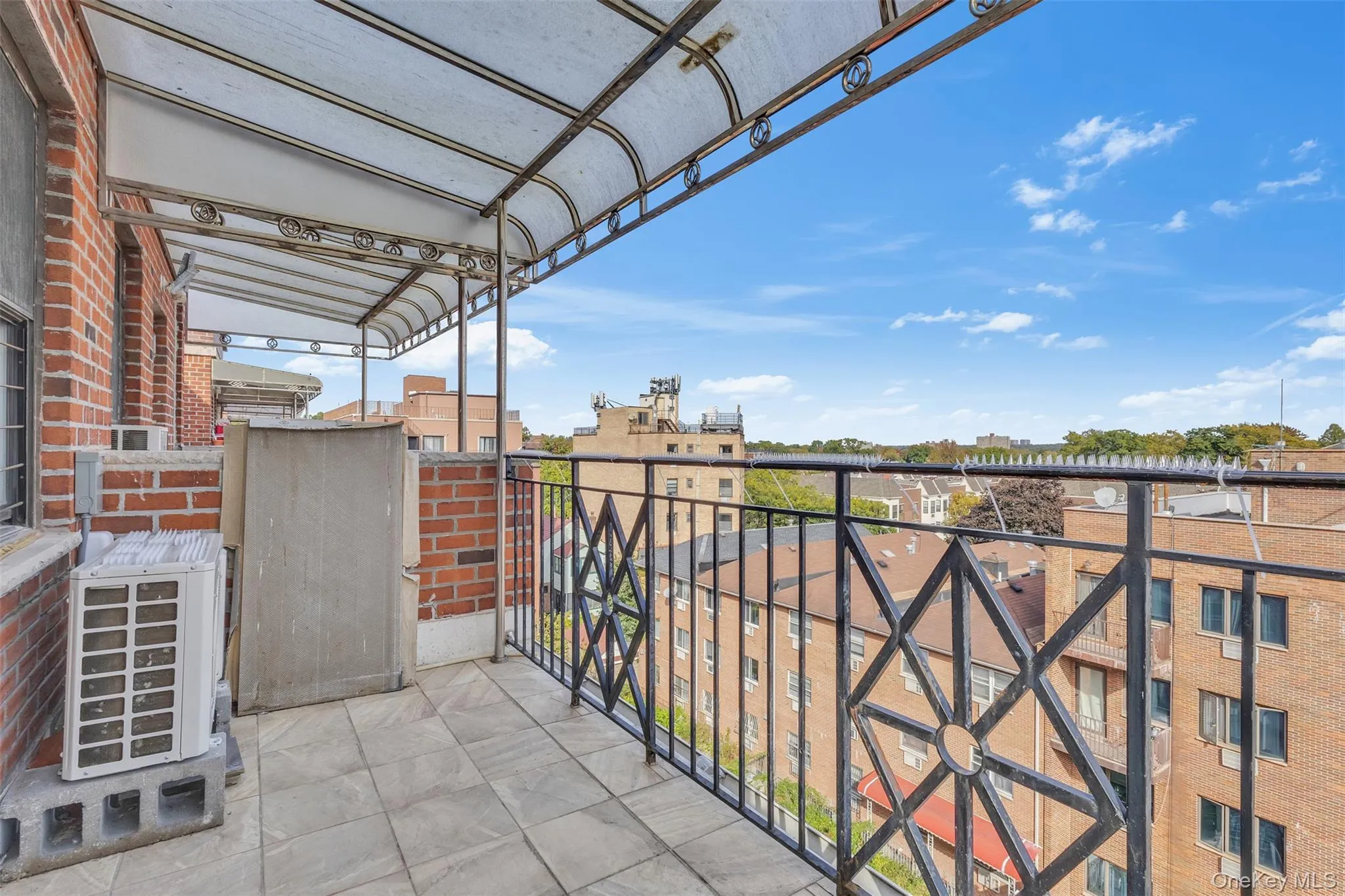 Private balcony featuring a geometric black metal railing, overhead awning, brick facade, and tile flooring Private balcony featuring a geometric black metal railing, overhead awning, brick facade, and tile flooring