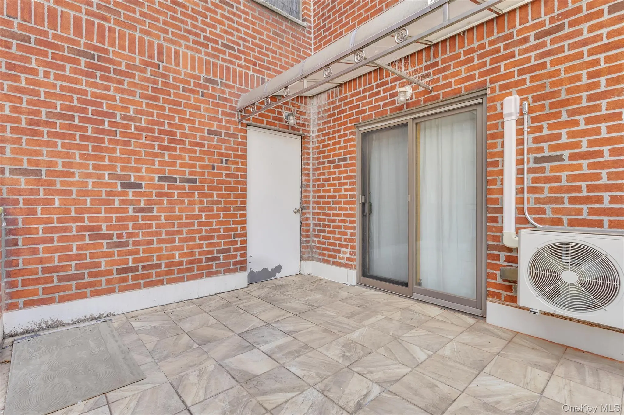 Outdoor terrace featuring red brick walls, tiled flooring, a sliding glass door, an attached metal awning, and wall-mounted exterior lighting Outdoor terrace featuring red brick walls, tiled flooring, a sliding glass door, an attached metal awning, and wall-mounted exterior lighting