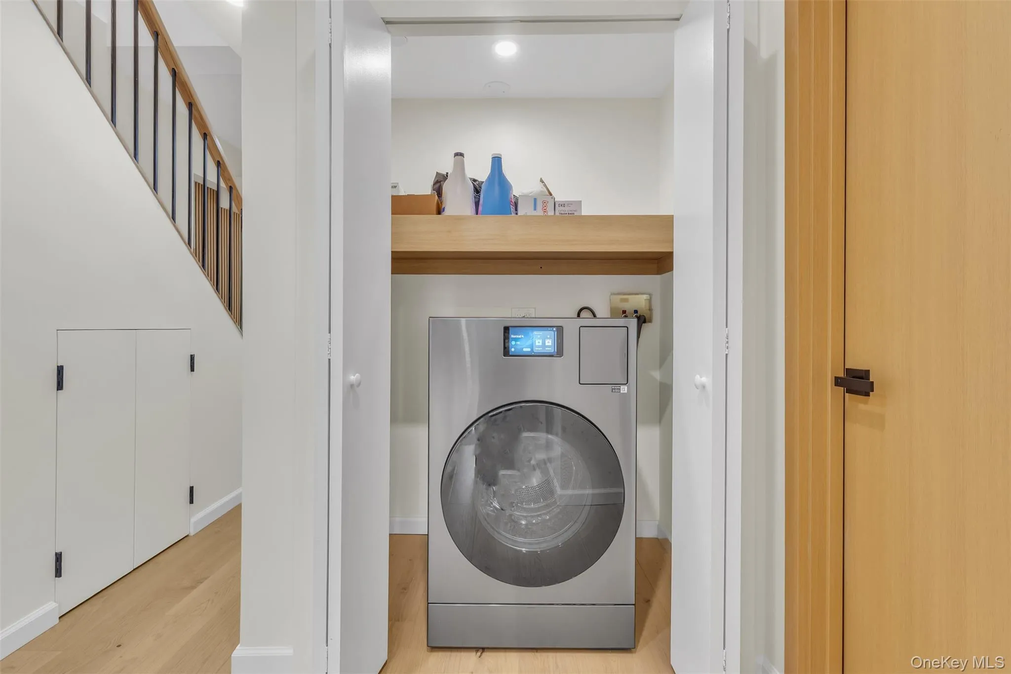Laundry closet featuring a stainless-steel washer-dryer combination unit, custom built-in wood shelving, wood-finish flooring, and double-hinged doors Laundry closet featuring a stainless-steel washer-dryer combination unit, custom built-in wood shelving, wood-finish flooring, and double-hinged doors