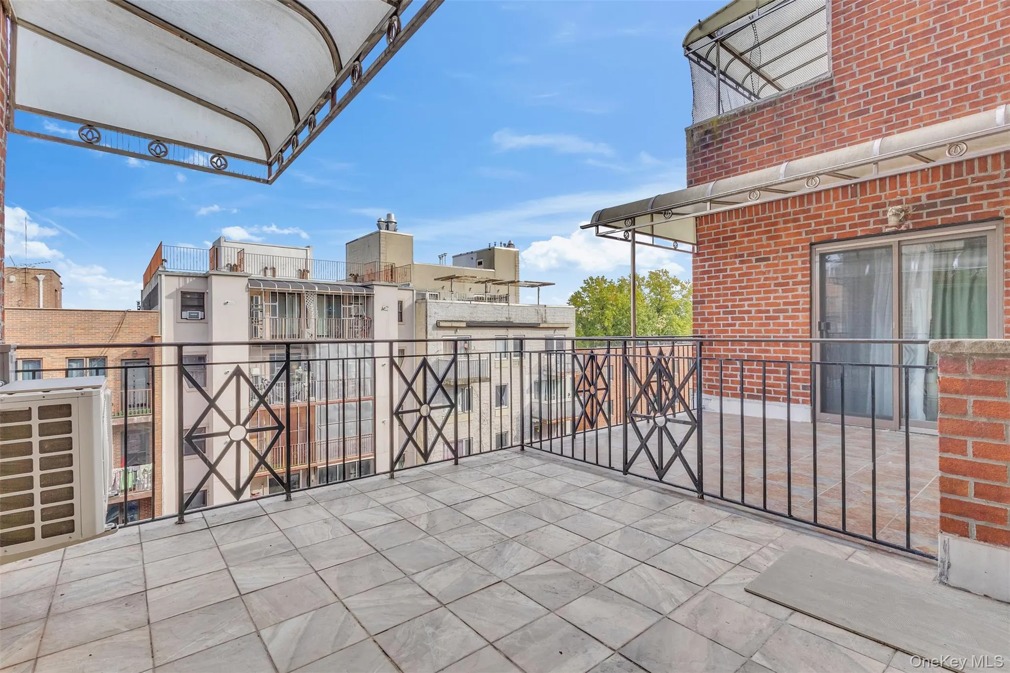 Spacious outdoor terrace featuring tiled flooring, wrought-iron railings, an overhead awning, and exterior brick masonry Spacious outdoor terrace featuring tiled flooring, wrought-iron railings, an overhead awning, and exterior brick masonry