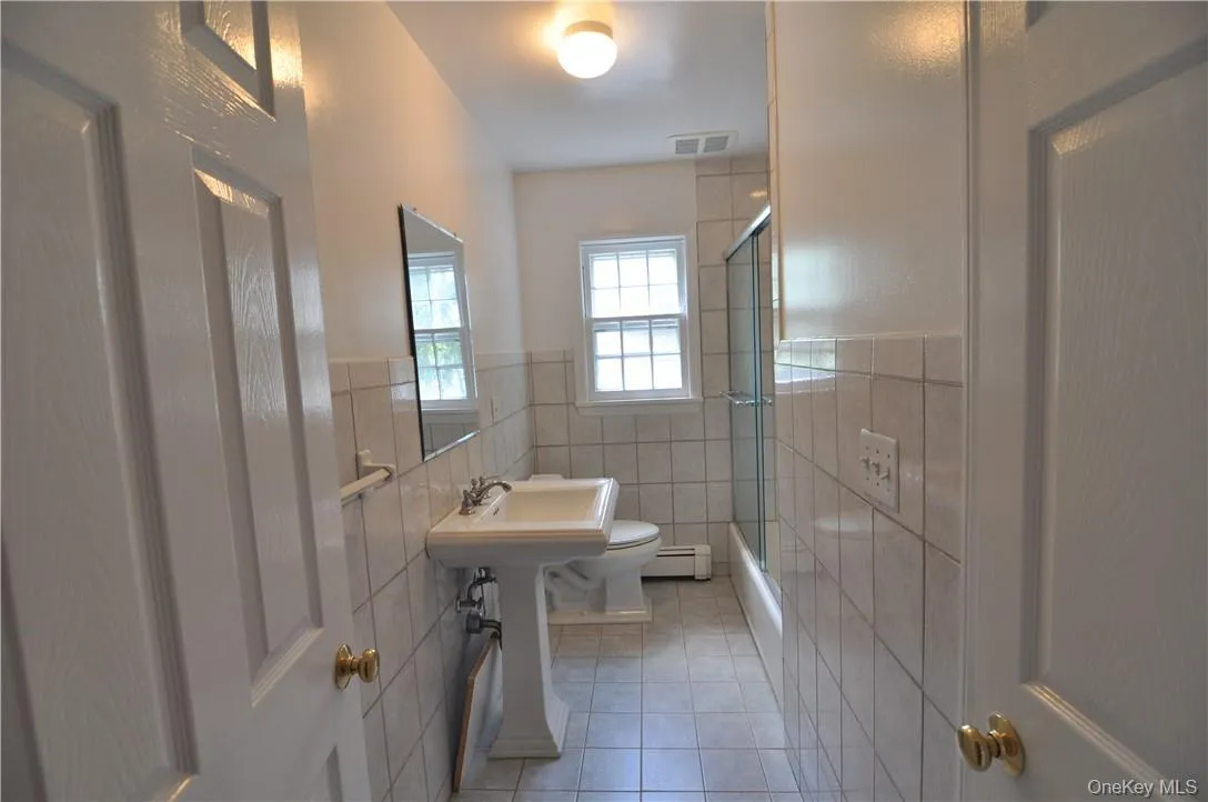Bathroom with tile patterned flooring, an enclosed shower, toilet, tile walls, and a baseboard radiator Bathroom with tile patterned flooring, an enclosed shower, toilet, tile walls, and a baseboard radiator