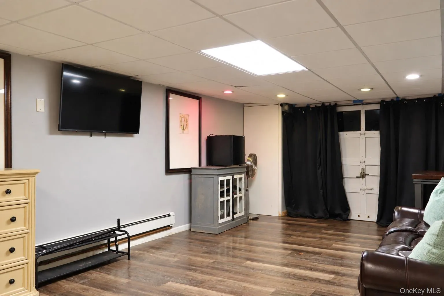 Finished space featuring wood-finish flooring, drop ceiling with recessed lighting, and wall-mounted television bracket Finished space featuring wood-finish flooring, drop ceiling with recessed lighting, and wall-mounted television bracket