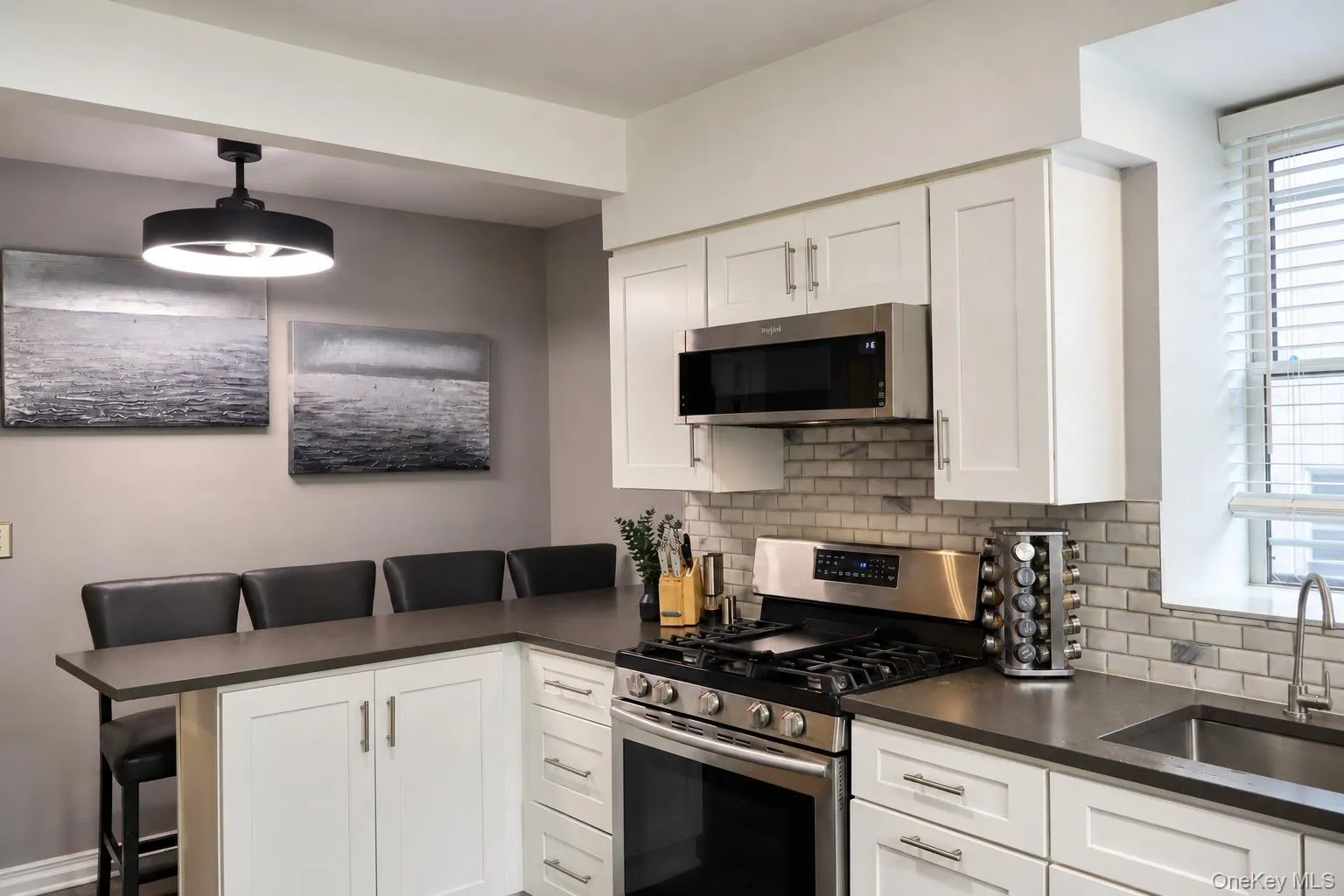 Kitchen featuring white Shaker-style cabinetry, dark solid-surface countertops, stainless steel appliances, subway tile backsplash, and a contemporary drum-style pendant light Kitchen featuring white Shaker-style cabinetry, dark solid-surface countertops, stainless steel appliances, subway tile backsplash, and a contemporary drum-style pendant light