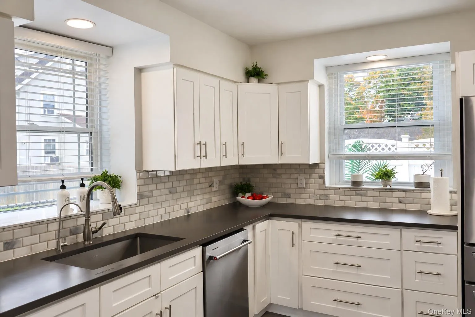 Kitchen featuring shaker-style cabinetry, dark solid-surface countertops, subway tile backsplash, stainless steel appliances, and dual windows Kitchen featuring shaker-style cabinetry, dark solid-surface countertops, subway tile backsplash, stainless steel appliances, and dual windows
