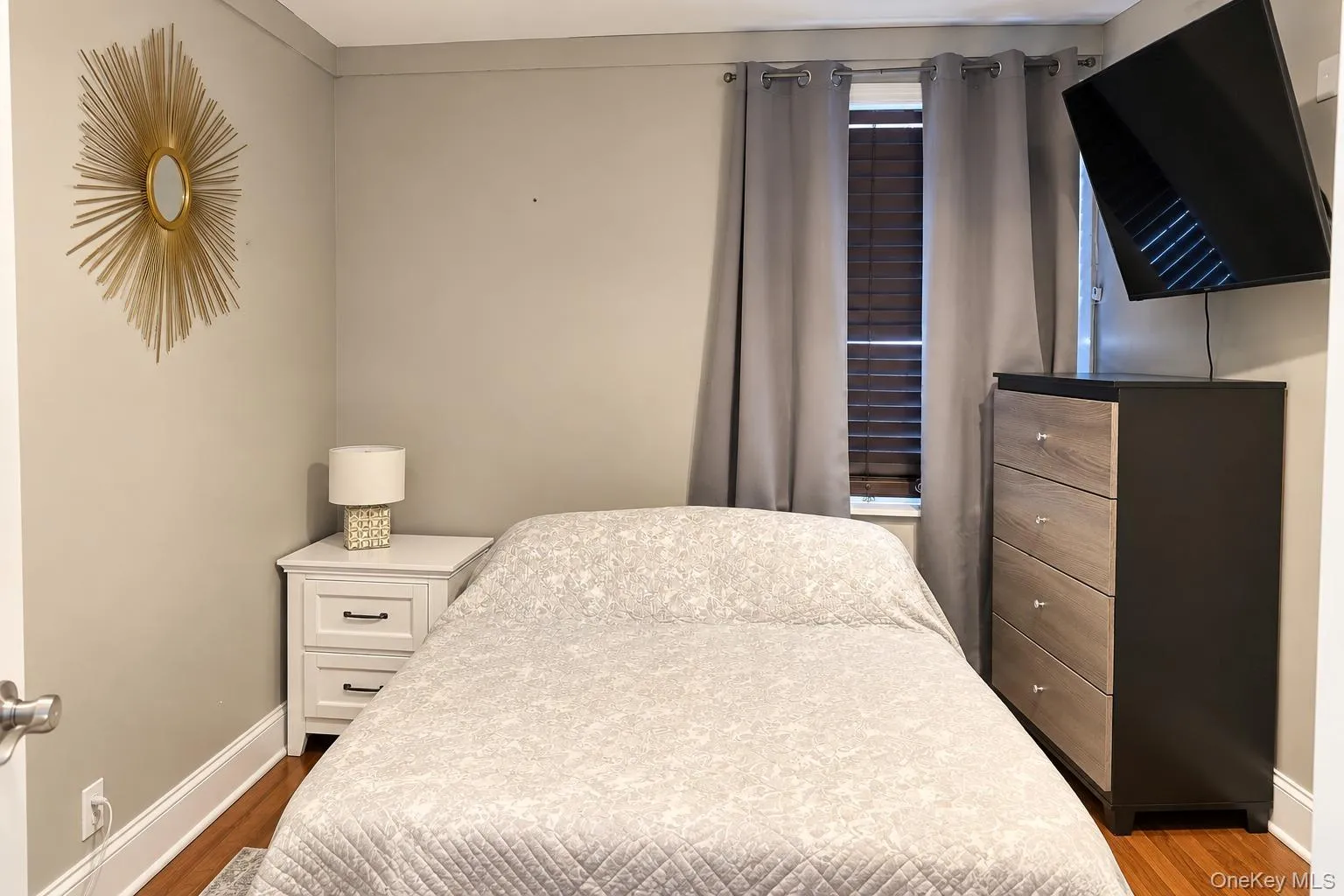 Room featuring wood-finish flooring, a window with horizontal blinds, and neutral wall paint Room featuring wood-finish flooring, a window with horizontal blinds, and neutral wall paint