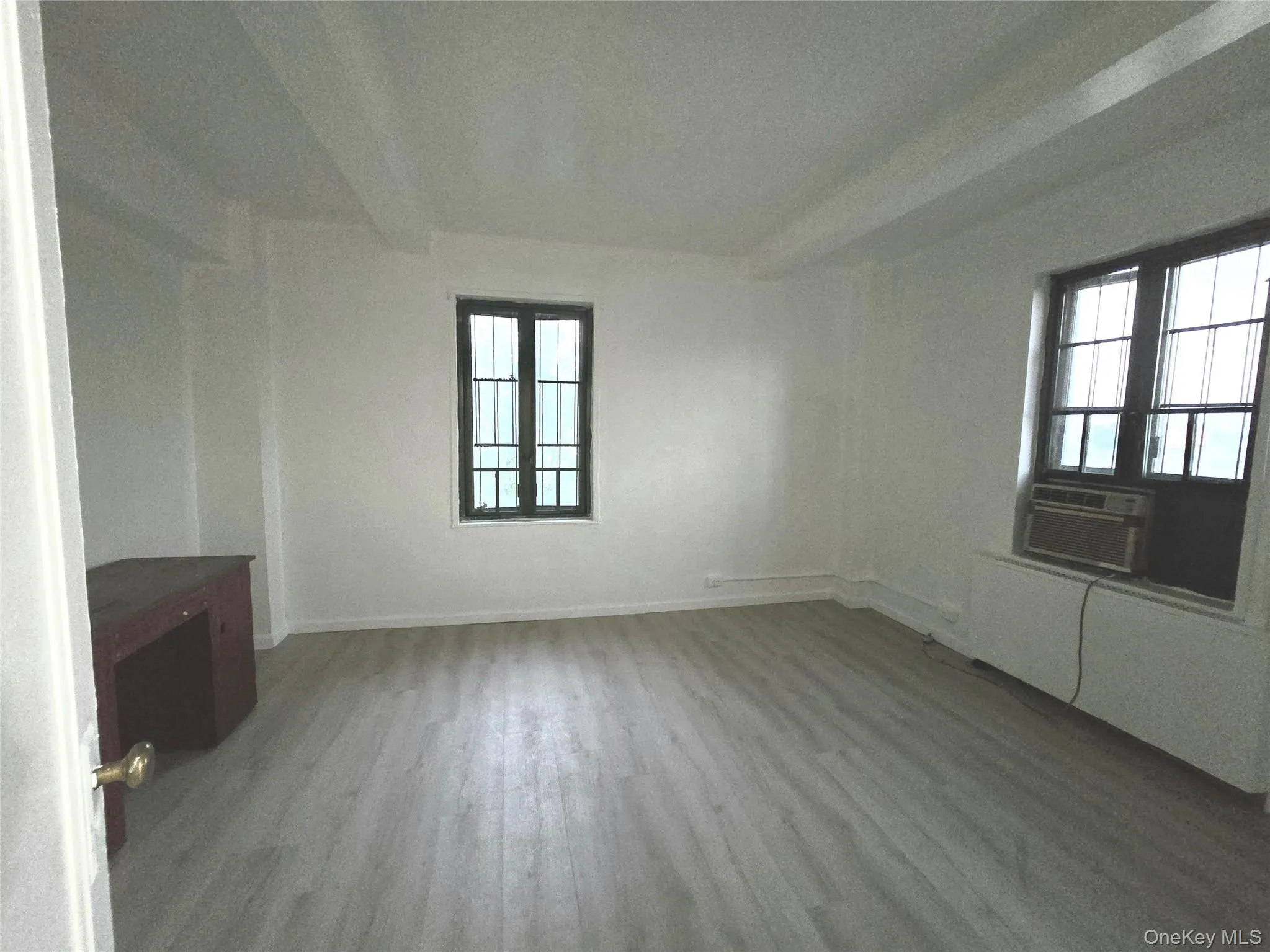 Neutral interior featuring wood-finish flooring, two-pane windows with grid detailing, and recessed beam ceiling architecture Neutral interior featuring wood-finish flooring, two-pane windows with grid detailing, and recessed beam ceiling architecture