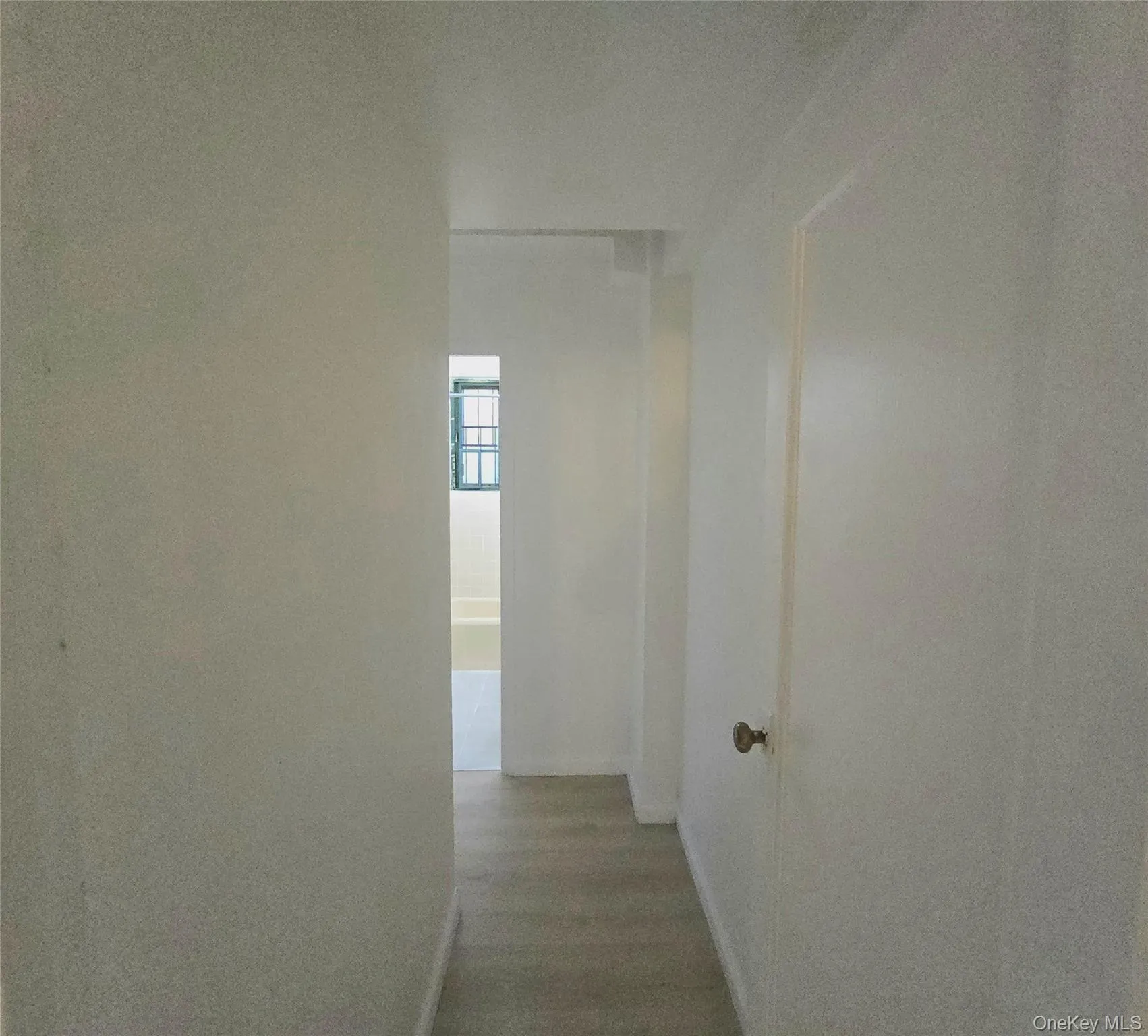 Hallway featuring wood-finish flooring and a white interior door with a round brass-finish knob Hallway featuring wood-finish flooring and a white interior door with a round brass-finish knob