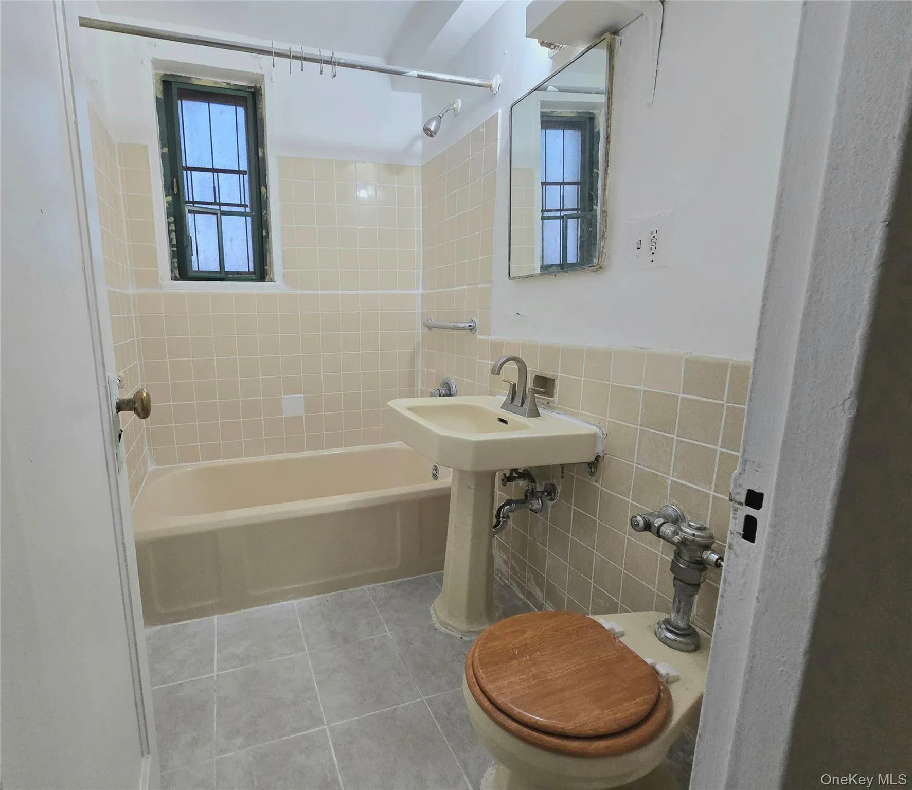 Bathroom featuring a porcelain pedestal sink with a metal faucet, a built-in bathtub, a window with metal framing, and wall-mounted tile backsplash Bathroom featuring a porcelain pedestal sink with a metal faucet, a built-in bathtub, a window with metal framing, and wall-mounted tile backsplash