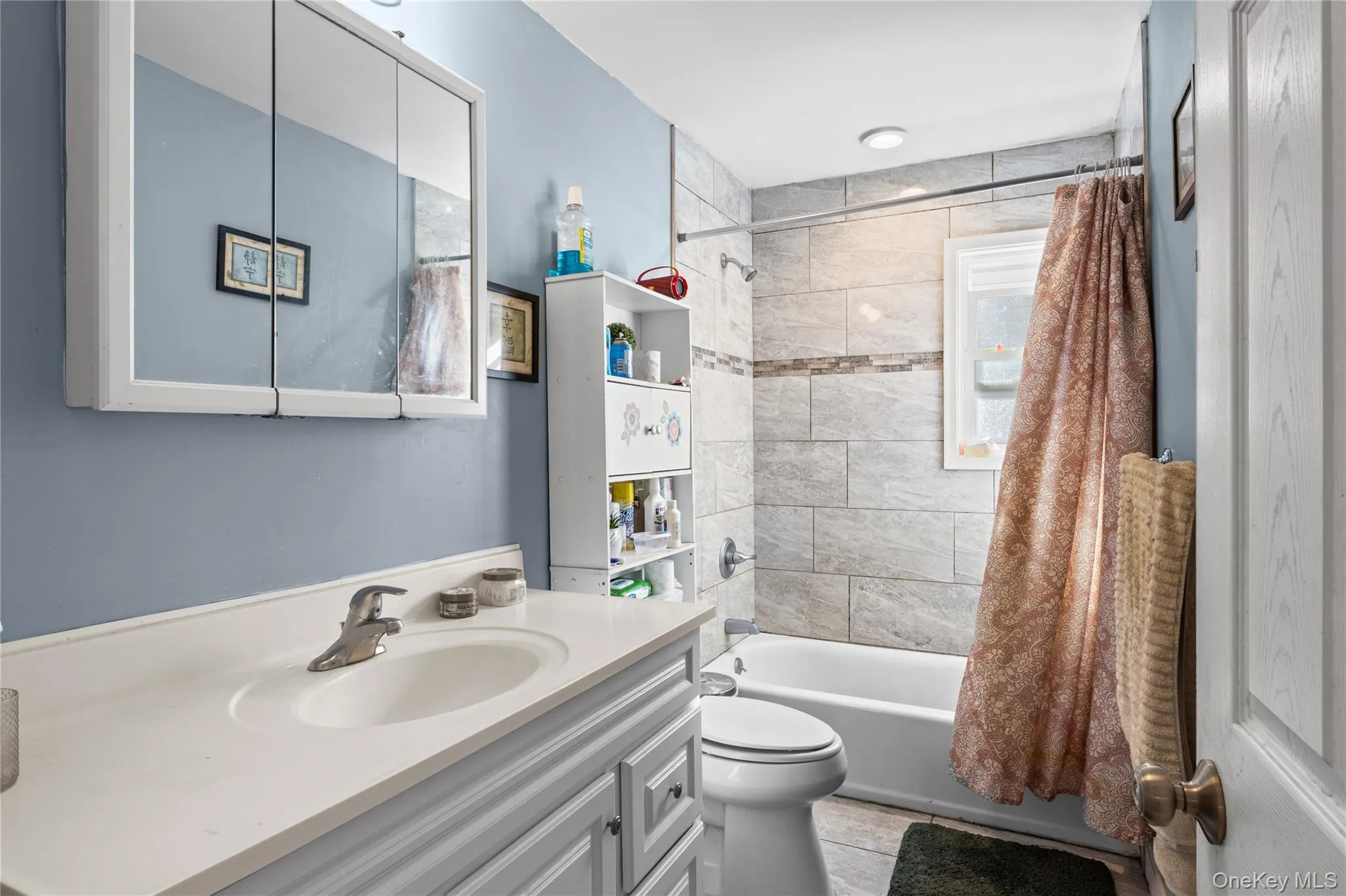 Bathroom featuring a vanity with an integrated sink, tri-fold medicine cabinet, tub-shower combination with tile surround, and wood-finish flooring Bathroom featuring a vanity with an integrated sink, tri-fold medicine cabinet, tub-shower combination with tile surround, and wood-finish flooring