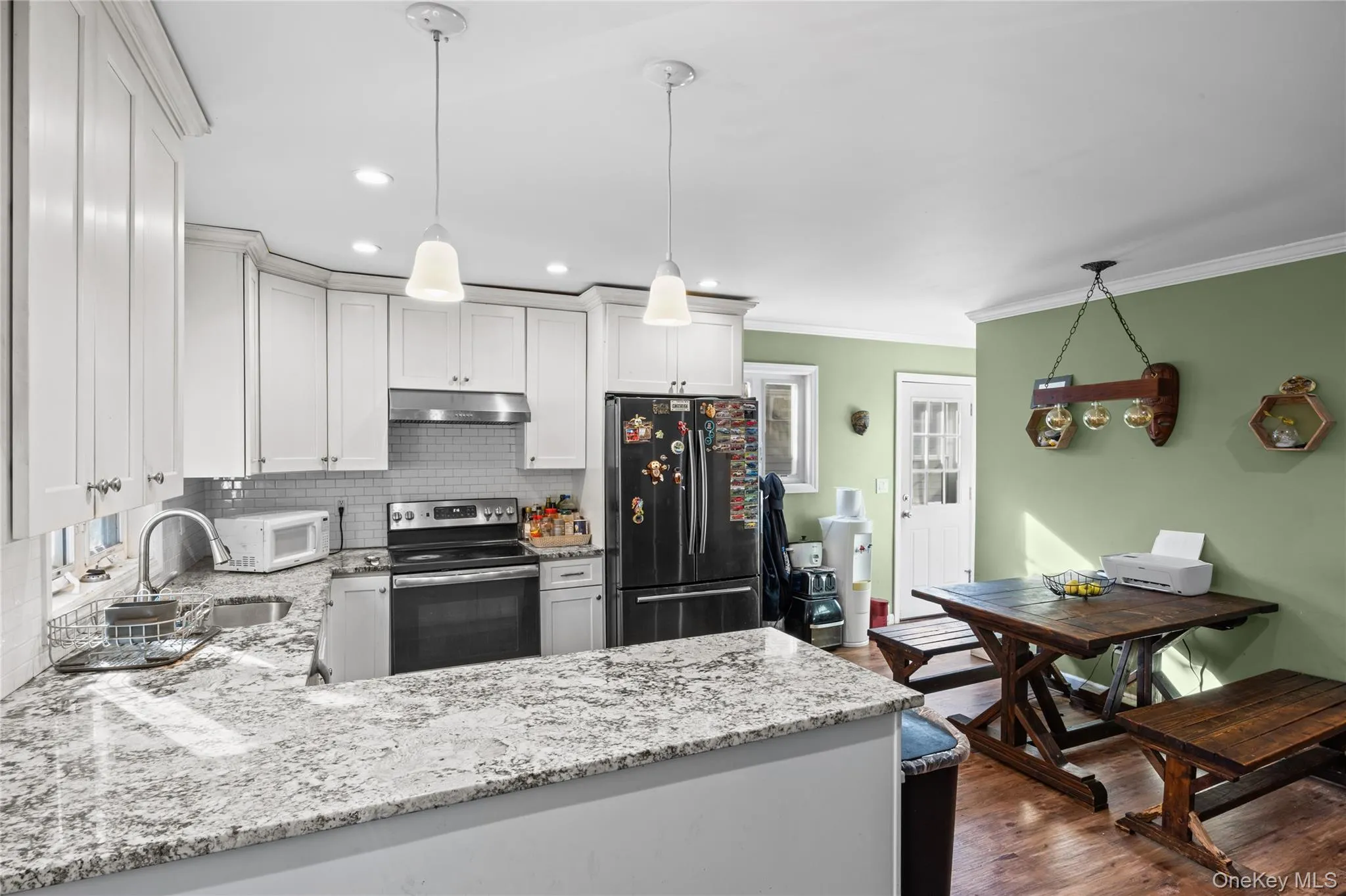 Kitchen featuring white shaker-style cabinetry, stone countertops, a subway tile backsplash, stainless steel appliances, and pendant lighting Kitchen featuring white shaker-style cabinetry, stone countertops, a subway tile backsplash, stainless steel appliances, and pendant lighting