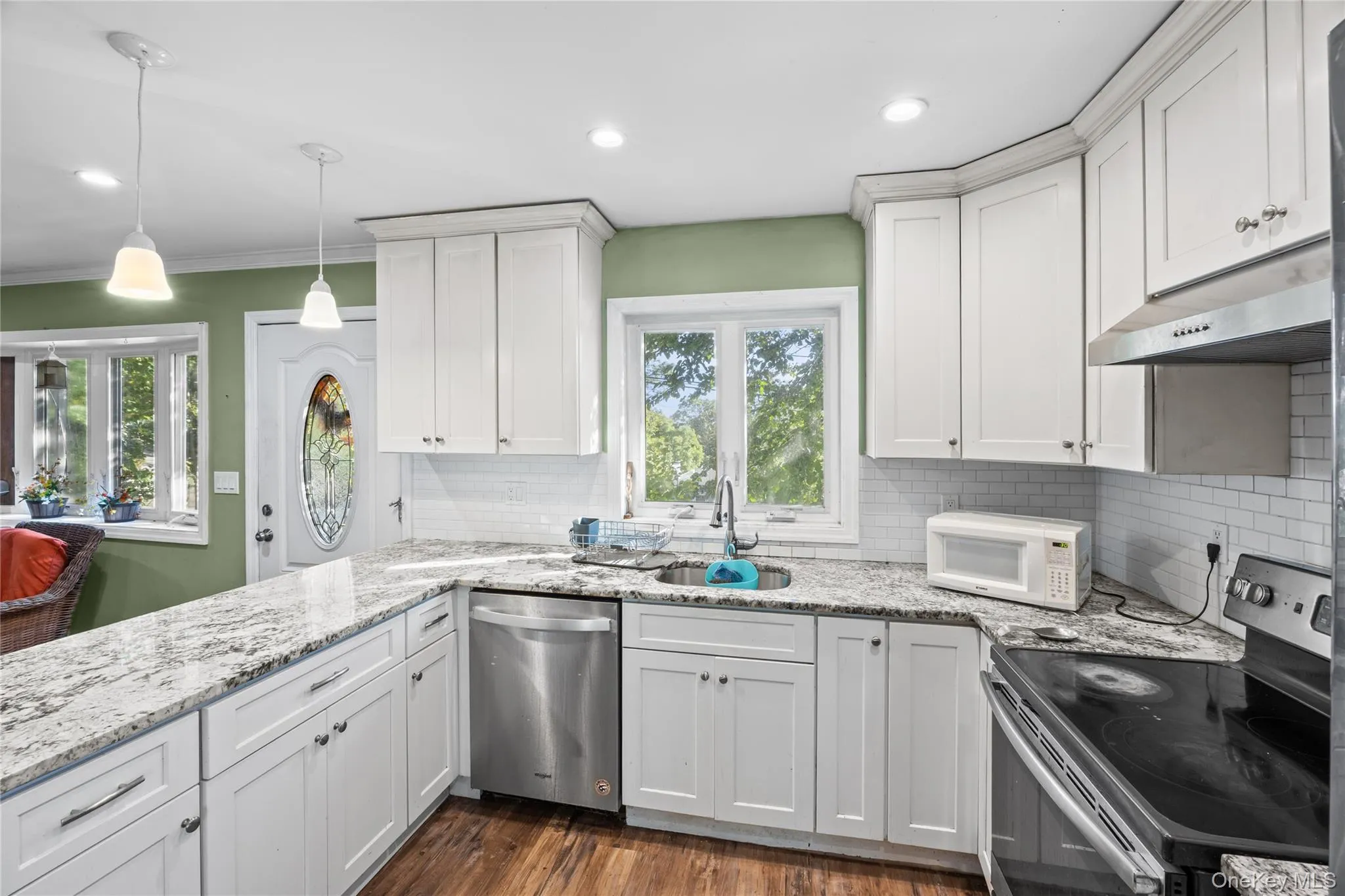 Kitchen featuring white shaker-style cabinetry, stone-patterned countertops, subway tile backsplash, stainless steel appliances, and wood-finish flooring Kitchen featuring white shaker-style cabinetry, stone-patterned countertops, subway tile backsplash, stainless steel appliances, and wood-finish flooring