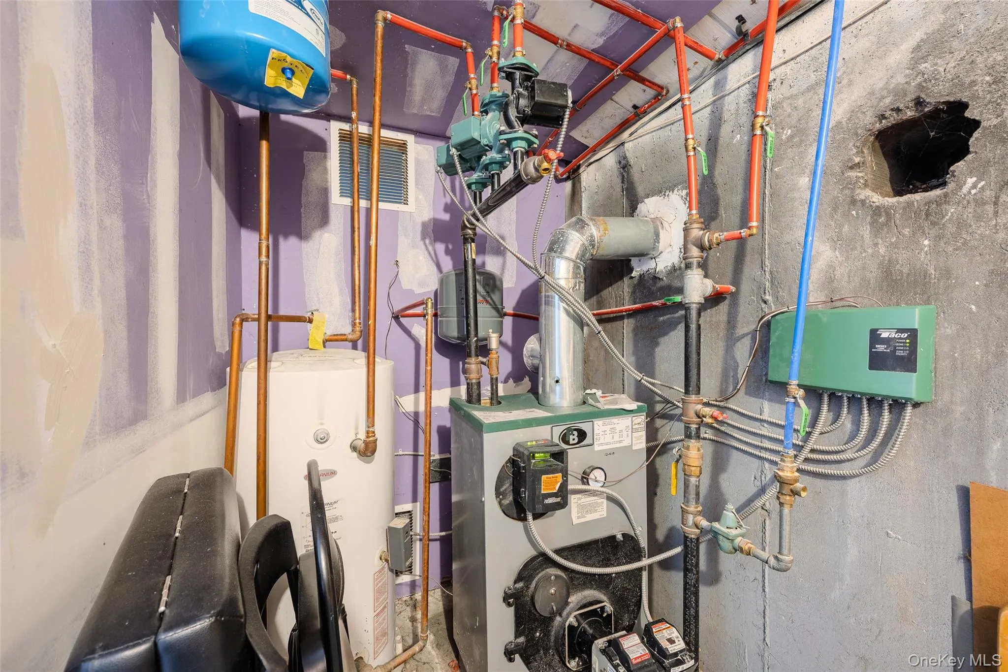 Mechanical room featuring a floor-standing boiler, vertical water storage tank, copper plumbing, circulator pump, and electrical zone control panel Mechanical room featuring a floor-standing boiler, vertical water storage tank, copper plumbing, circulator pump, and electrical zone control panel