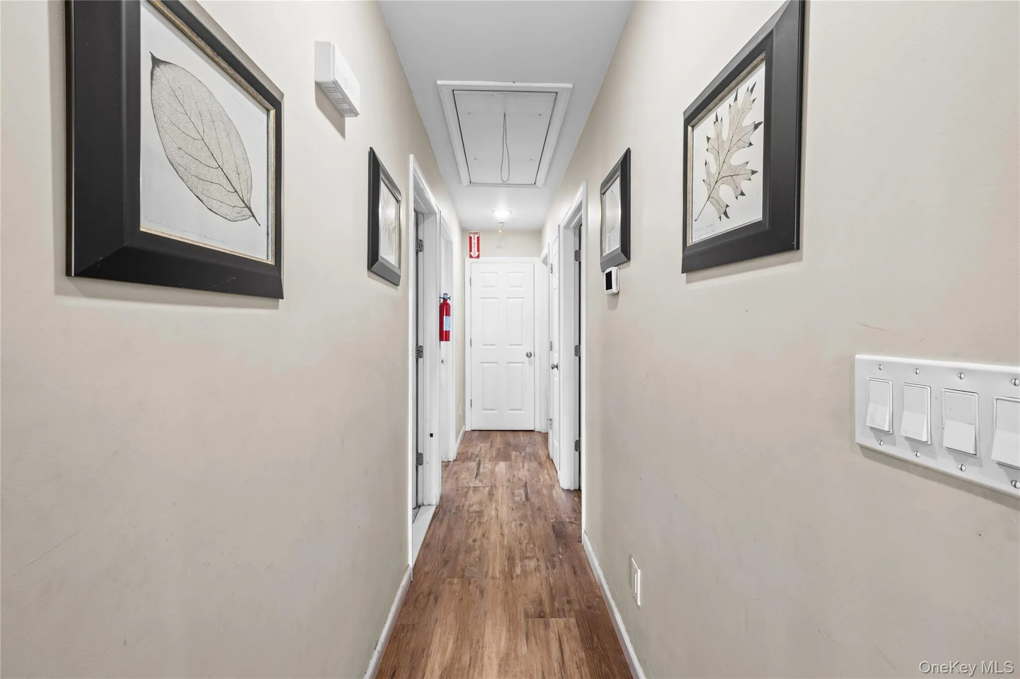 Hallway featuring wood-finish flooring, neutral wall paint, and multiple interior doors Hallway featuring wood-finish flooring, neutral wall paint, and multiple interior doors