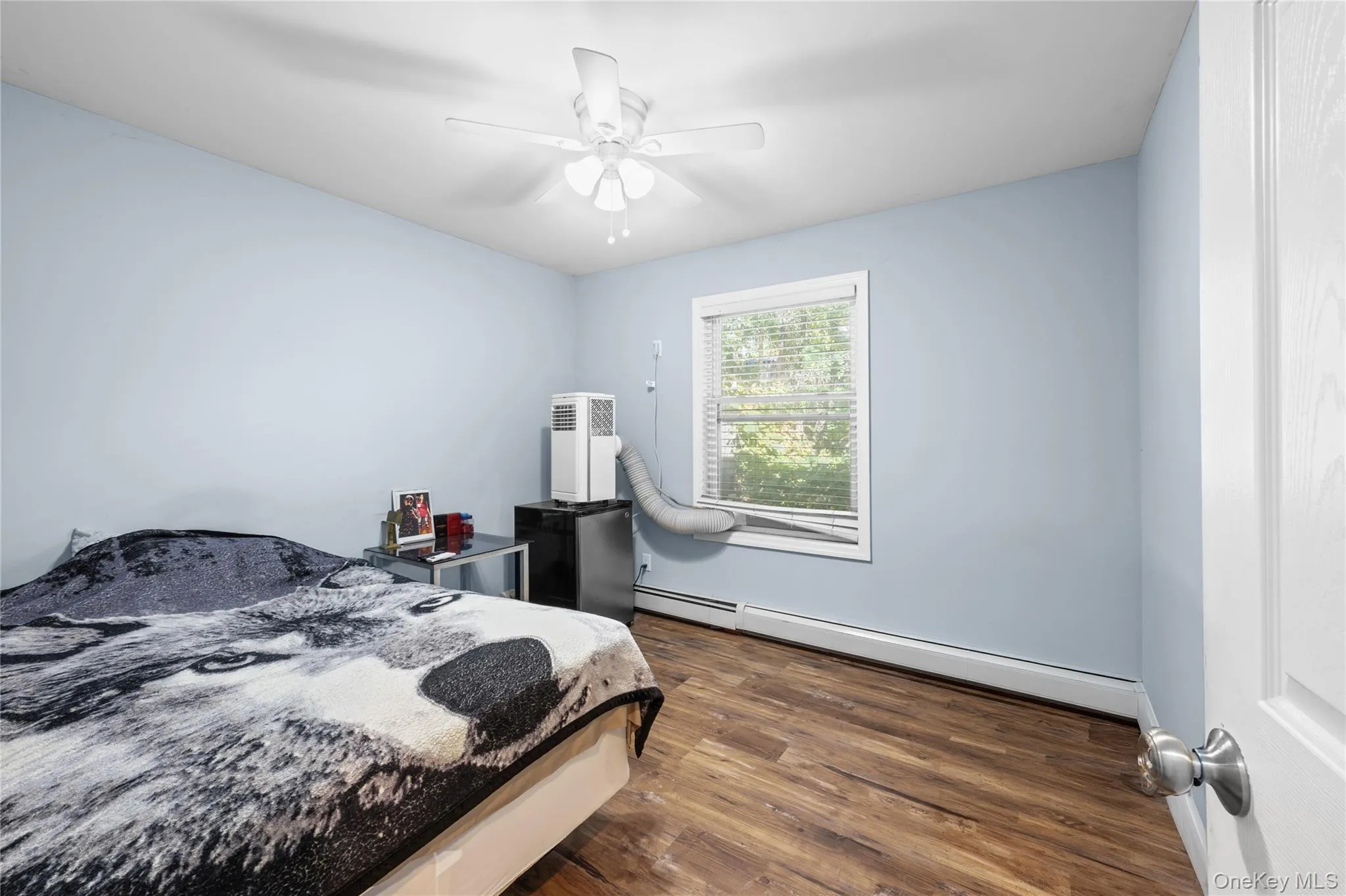 Room featuring wood-finish flooring, a multi-blade ceiling fan with integrated lighting, and a window with horizontal blinds Room featuring wood-finish flooring, a multi-blade ceiling fan with integrated lighting, and a window with horizontal blinds