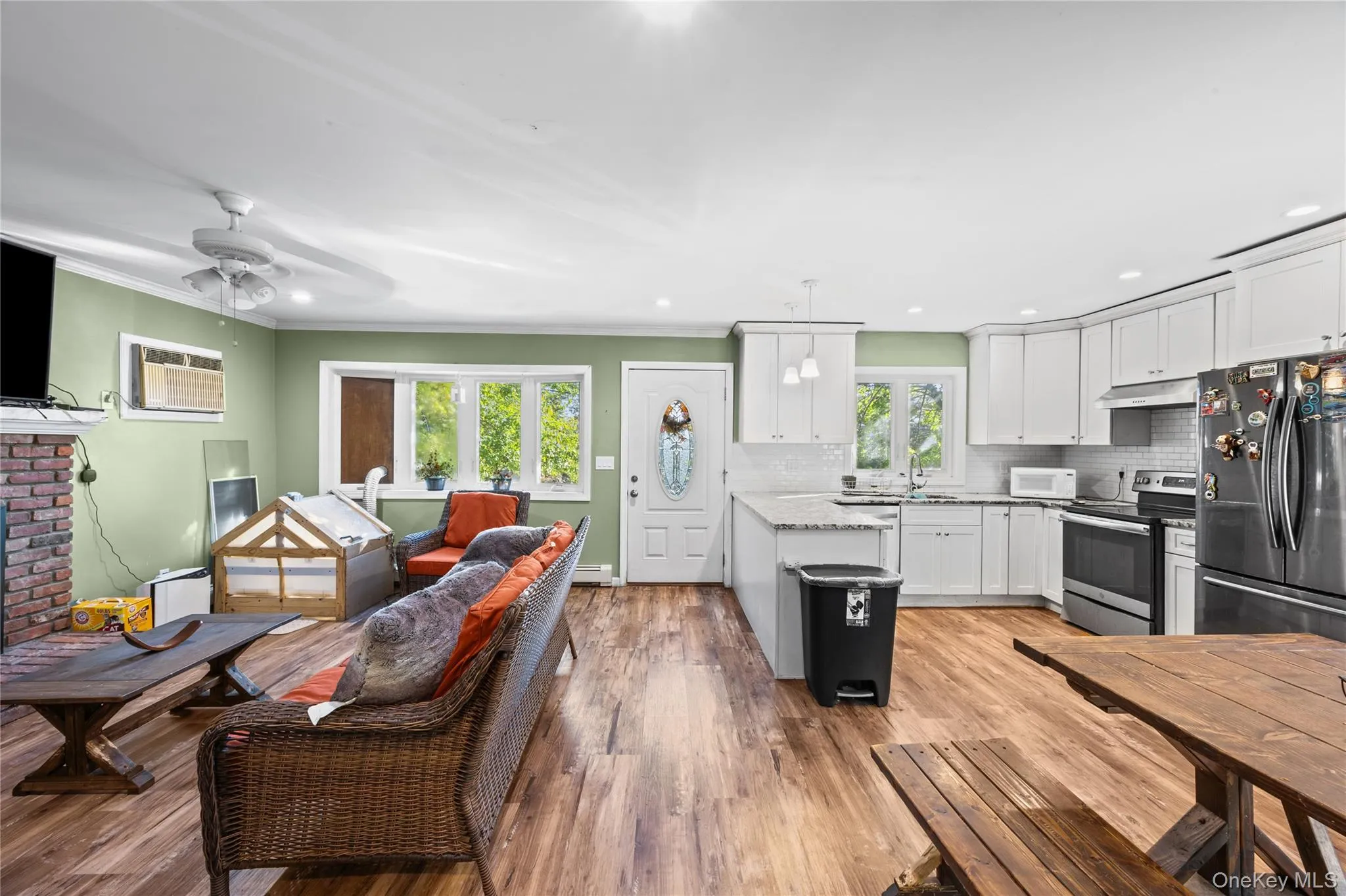 Open-concept living space featuring wood-finish flooring, white cabinetry with stone countertops, a brick fireplace surround, and recessed lighting Open-concept living space featuring wood-finish flooring, white cabinetry with stone countertops, a brick fireplace surround, and recessed lighting