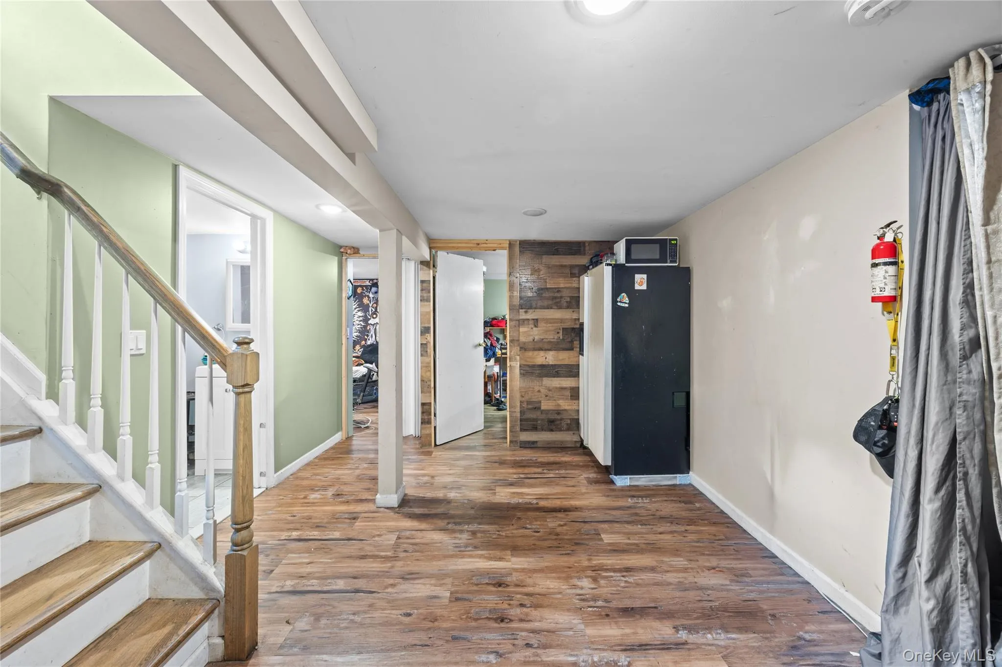 Interior space featuring wood-finish flooring, a wood-plank accent wall, and a staircase with a wooden handrail and white balusters Interior space featuring wood-finish flooring, a wood-plank accent wall, and a staircase with a wooden handrail and white balusters