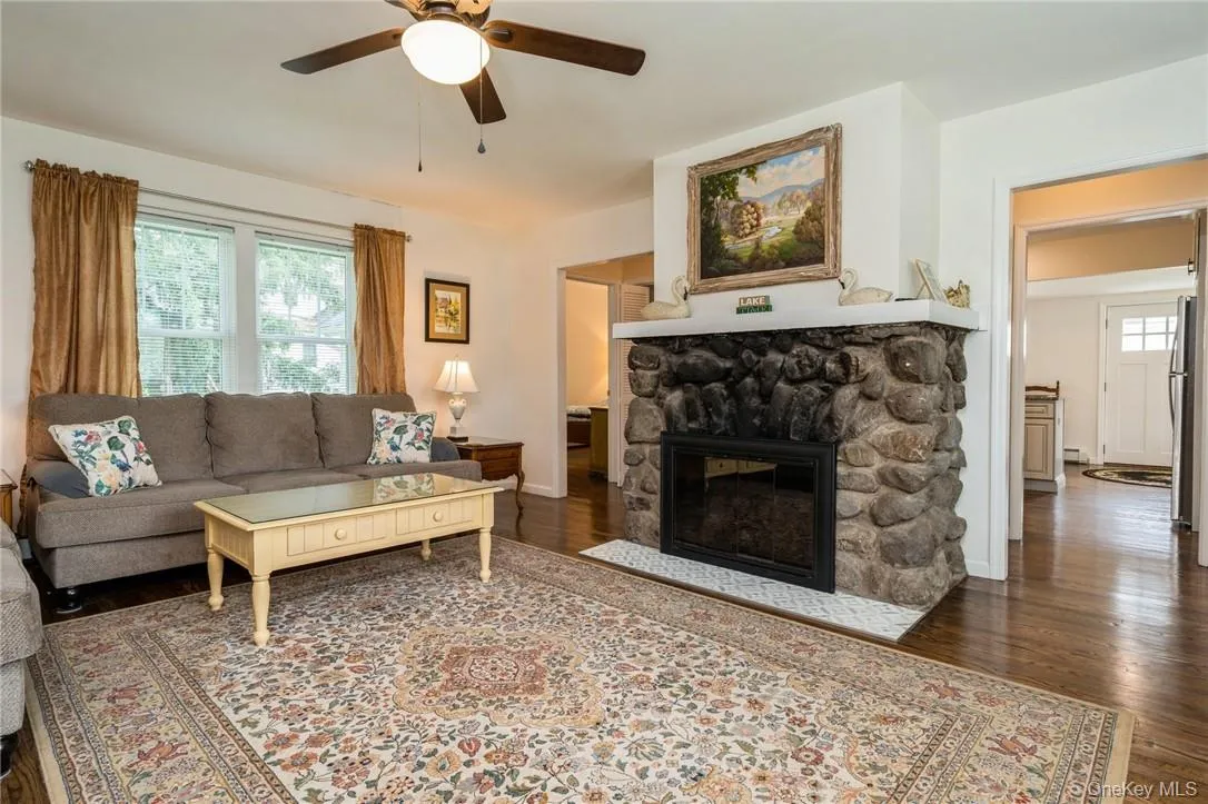 Living room featuring a stone fireplace, ceiling fan, and dark hardwood / wood-style flooring Living room featuring a stone fireplace, ceiling fan, and dark hardwood / wood-style flooring
