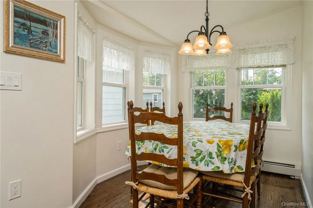 Dining room featuring lofted ceiling, a notable chandelier, baseboard heating, and dark wood-type flooring Dining room featuring lofted ceiling, a notable chandelier, baseboard heating, and dark wood-type flooring