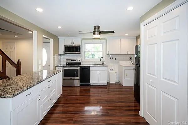 Kitchen with white cabinetry, black appliances, dark wood finished floors, washer / clothes dryer, and recessed lighting Kitchen with white cabinetry, black appliances, dark wood finished floors, washer / clothes dryer, and recessed lighting