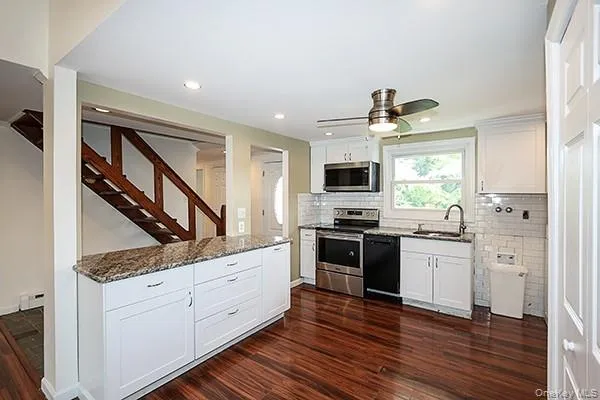 Kitchen featuring white cabinetry, stainless steel appliances, dark stone counters, dark wood-style flooring, and decorative backsplash Kitchen featuring white cabinetry, stainless steel appliances, dark stone counters, dark wood-style flooring, and decorative backsplash