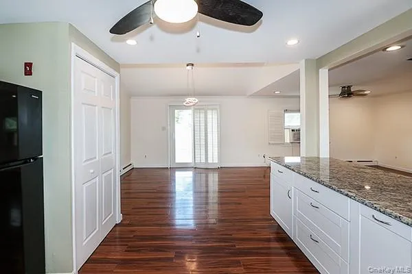 Kitchen featuring light stone counters, a ceiling fan, freestanding refrigerator, open floor plan, and dark wood-style floors Kitchen featuring light stone counters, a ceiling fan, freestanding refrigerator, open floor plan, and dark wood-style floors