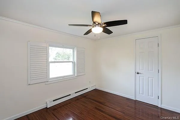 Empty room featuring crown molding, a baseboard heating unit, dark wood-style flooring, and a ceiling fan Empty room featuring crown molding, a baseboard heating unit, dark wood-style flooring, and a ceiling fan