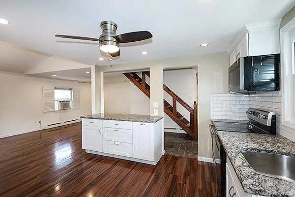 Kitchen featuring stainless steel appliances, white cabinetry, dark stone countertops, dark wood-type flooring, and recessed lighting Kitchen featuring stainless steel appliances, white cabinetry, dark stone countertops, dark wood-type flooring, and recessed lighting