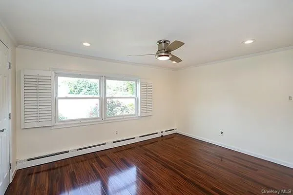 Spare room with a baseboard radiator, dark wood-style flooring, crown molding, a ceiling fan, and recessed lighting Spare room with a baseboard radiator, dark wood-style flooring, crown molding, a ceiling fan, and recessed lighting
