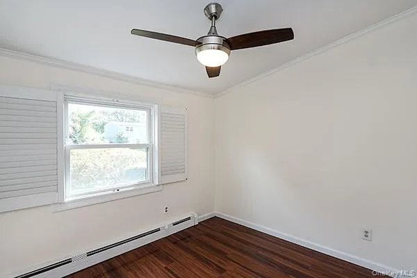 Empty room with a baseboard radiator, ornamental molding, dark wood-style floors, and a ceiling fan Empty room with a baseboard radiator, ornamental molding, dark wood-style floors, and a ceiling fan