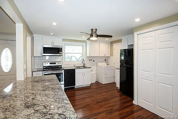 Kitchen featuring black appliances, white cabinetry, washer / dryer, dark wood-style flooring, and recessed lighting Kitchen featuring black appliances, white cabinetry, washer / dryer, dark wood-style flooring, and recessed lighting
