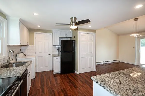 Kitchen with light stone countertops, white cabinets, tasteful backsplash, black appliances, and dark wood-style floors Kitchen with light stone countertops, white cabinets, tasteful backsplash, black appliances, and dark wood-style floors
