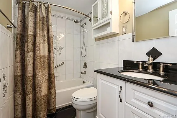 Bathroom with shower / bath combo, tile walls, vanity, dark tile patterned flooring, and decorative backsplash Bathroom with shower / bath combo, tile walls, vanity, dark tile patterned flooring, and decorative backsplash