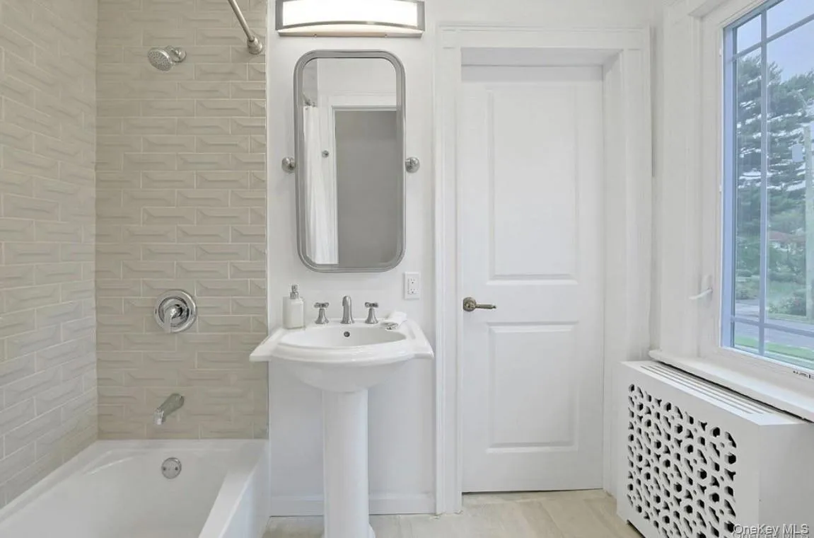 Bathroom featuring a pedestal sink, wall-mounted mirror, tub Bathroom featuring a pedestal sink, wall-mounted mirror, tub