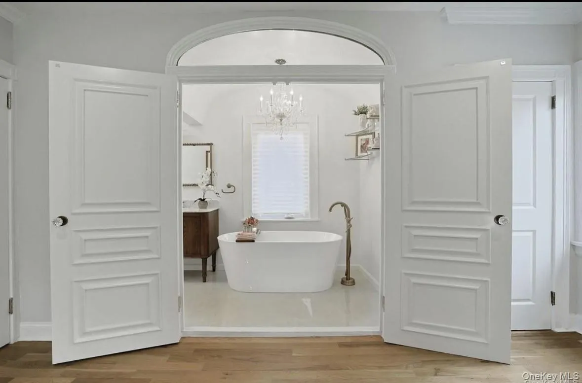 Double French doors with an arched transom, freestanding soaking tub, bronze floor-mounted faucet, crystal chandelier Double French doors with an arched transom, freestanding soaking tub, bronze floor-mounted faucet, crystal chandelier