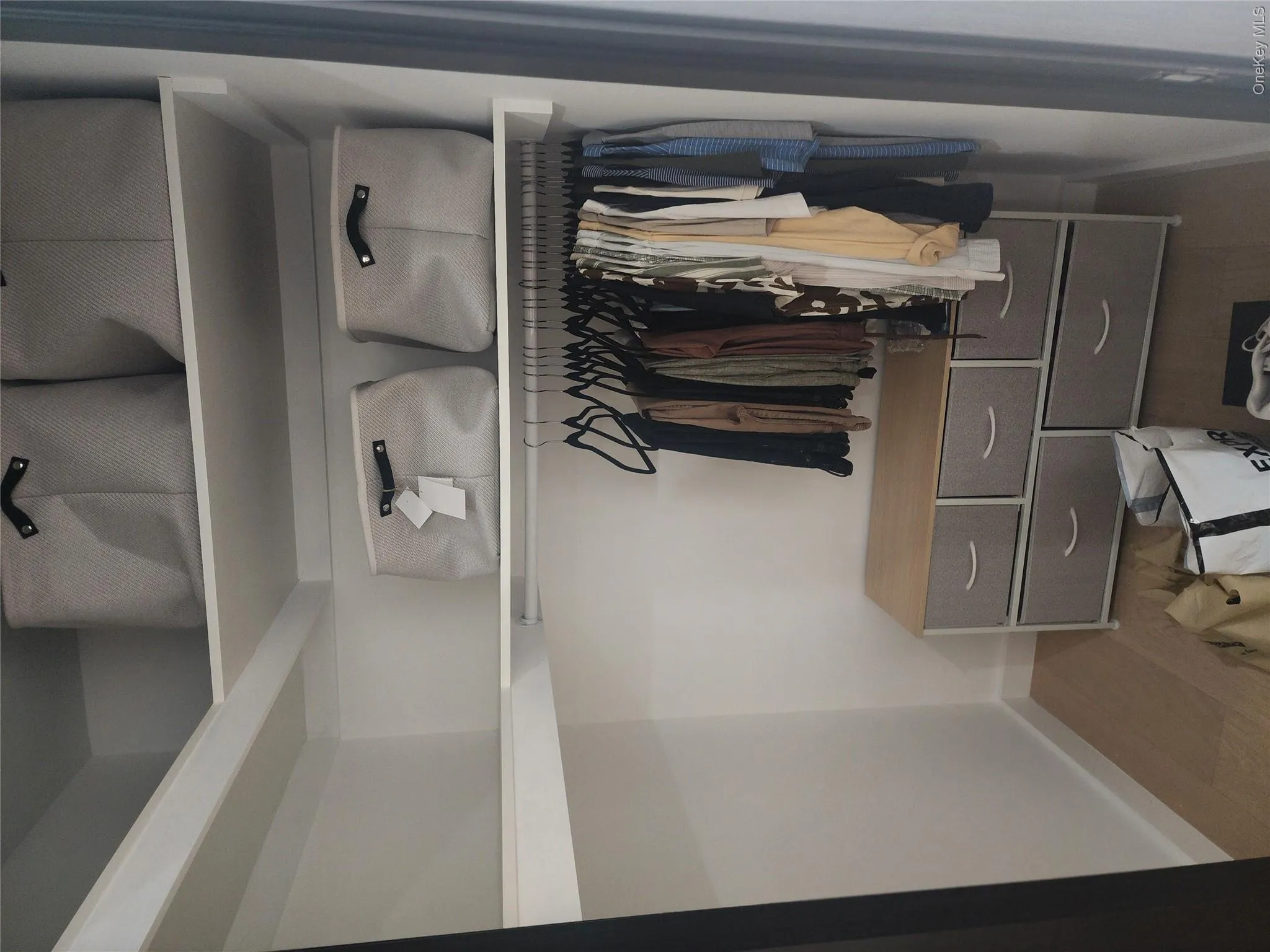 Storage closet featuring white-finish shelving, an integrated hanging rod, and light wood-finish flooring Storage closet featuring white-finish shelving, an integrated hanging rod, and light wood-finish flooring