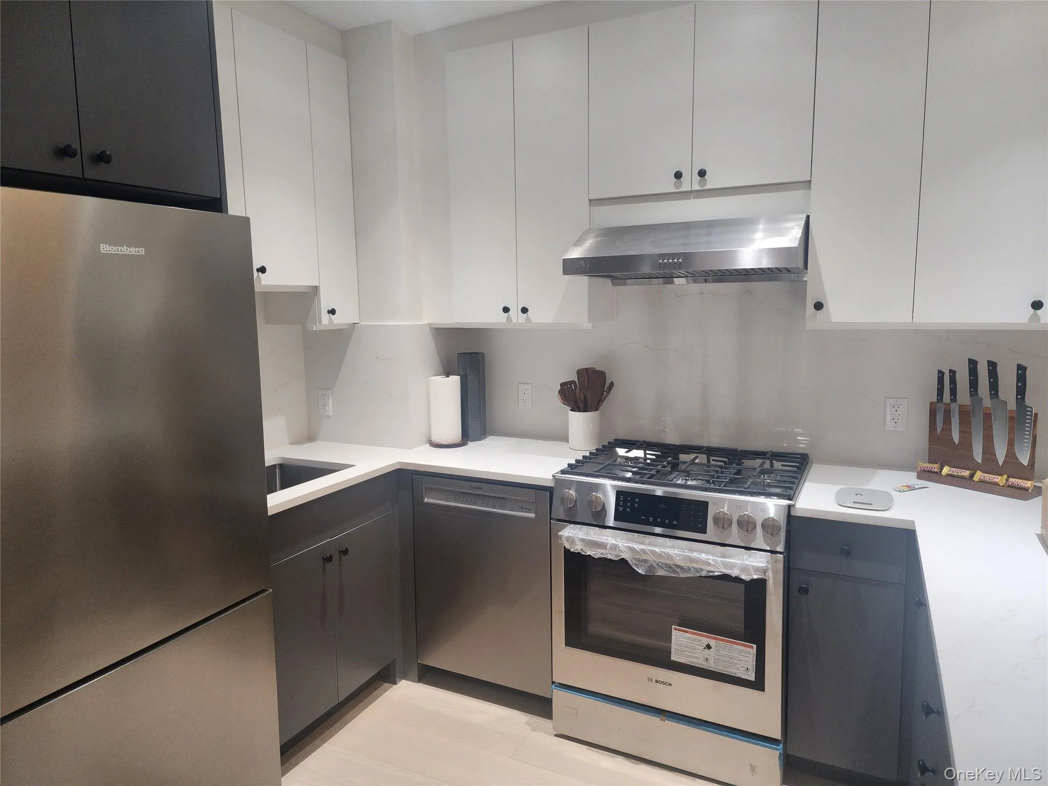 Kitchen featuring white and dark gray cabinetry, stone countertops, stainless steel appliances, and a gas range with a matching vent hood Kitchen featuring white and dark gray cabinetry, stone countertops, stainless steel appliances, and a gas range with a matching vent hood