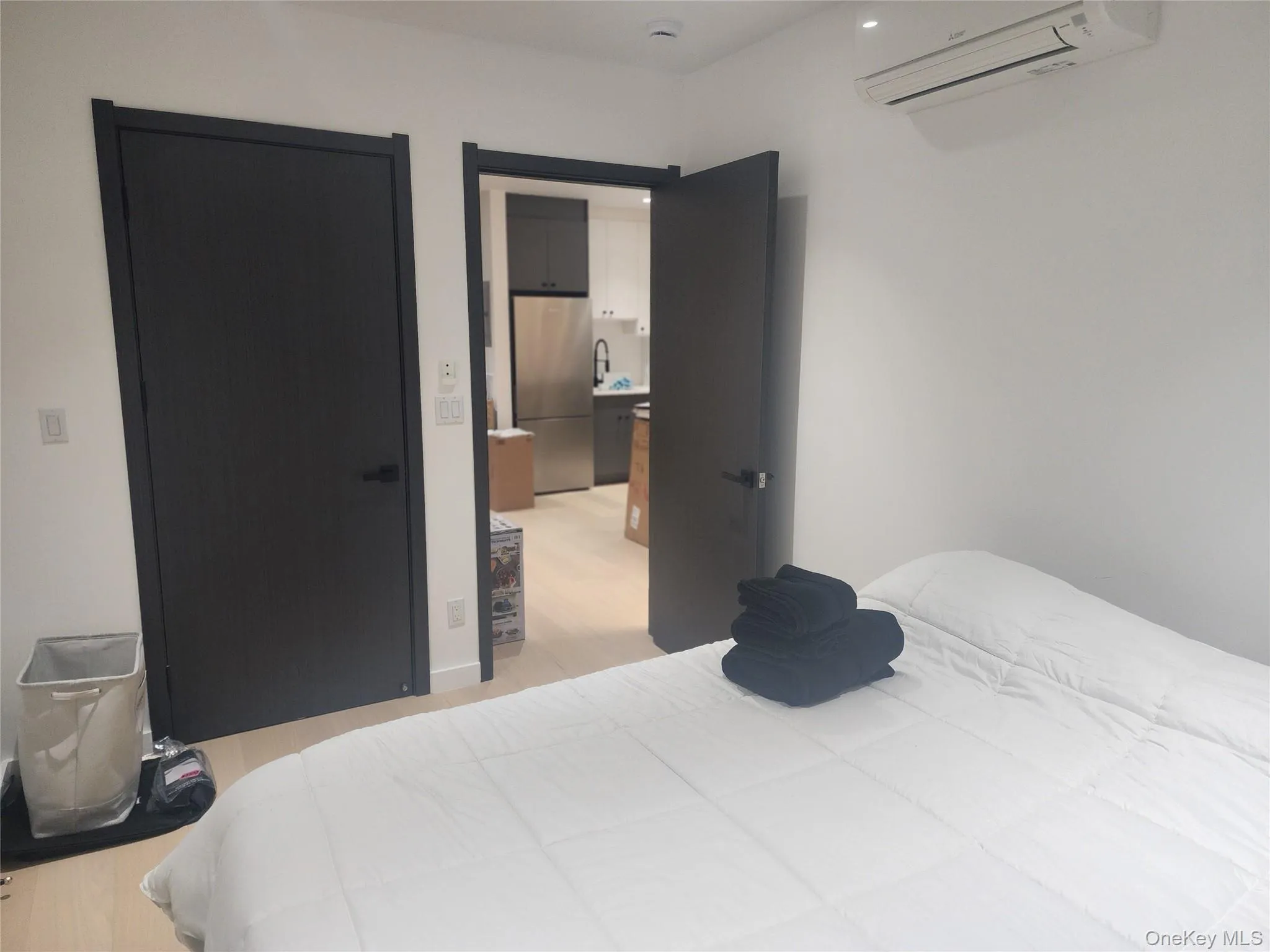 Neutral-toned interior featuring wood-finish flooring, dark-stained wood doors with matte black hardware, and a wall-mounted ductless climate control unit Neutral-toned interior featuring wood-finish flooring, dark-stained wood doors with matte black hardware, and a wall-mounted ductless climate control unit