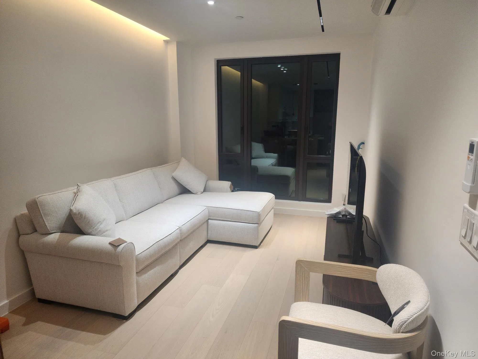 Interior space featuring wood-finish flooring, recessed ceiling lighting, cove lighting, and floor-to-ceiling dark-frame glass doors Interior space featuring wood-finish flooring, recessed ceiling lighting, cove lighting, and floor-to-ceiling dark-frame glass doors
