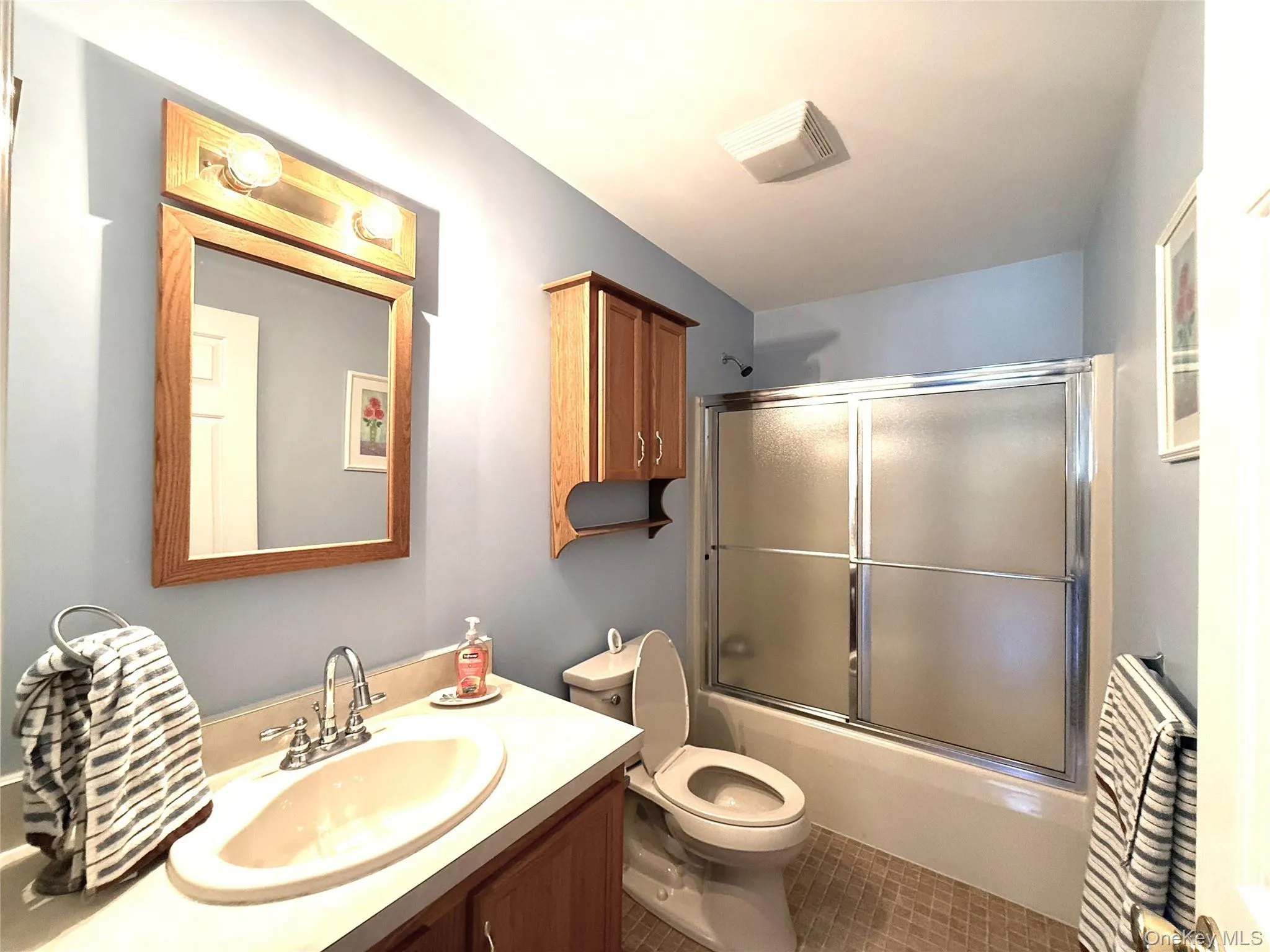 Bathroom featuring a wood-frame wall mirror, built-in wooden cabinetry, a solid-surface vanity countertop with an integrated basin, and a tub-shower combination with sliding frosted-glass doors Bathroom featuring a wood-frame wall mirror, built-in wooden cabinetry, a solid-surface vanity countertop with an integrated basin, and a tub-shower combination with sliding frosted-glass doors